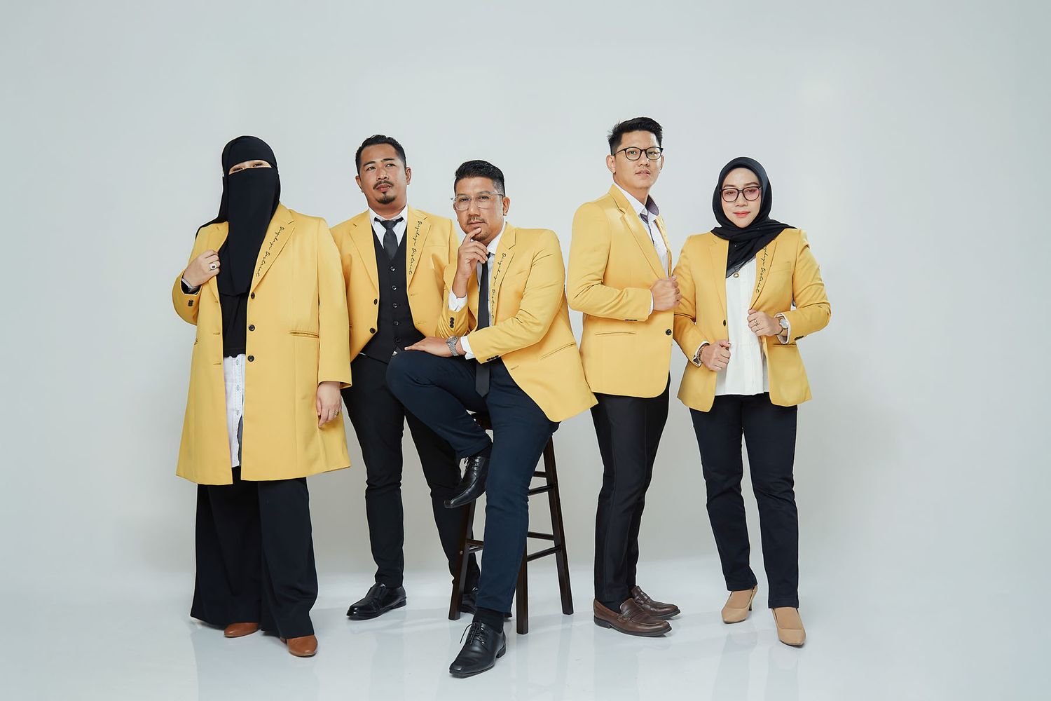 Five university students in matching yellow blazers pose confidently against white background in group photo.