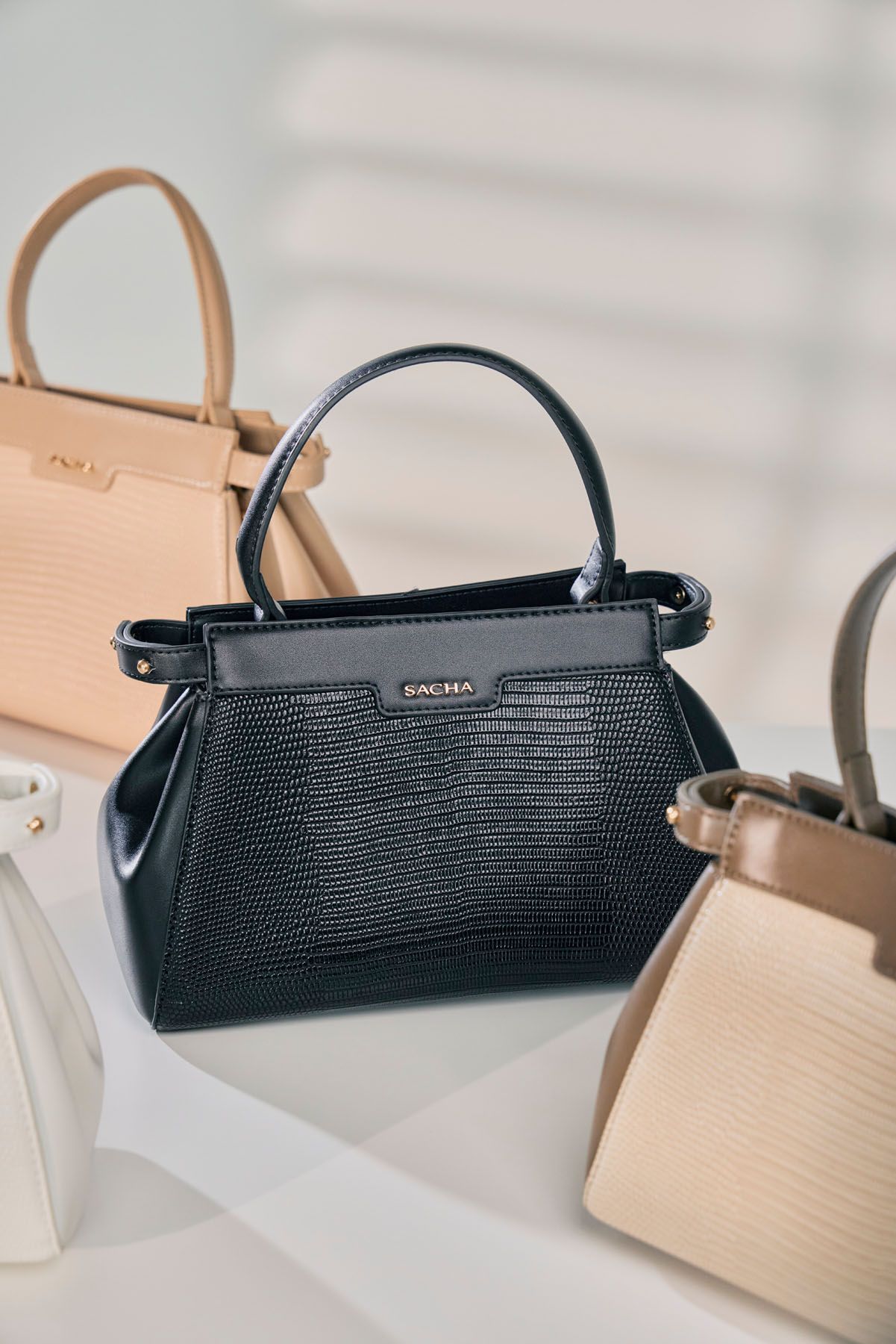 Black lizard-textured leather Sacma mini handbag surrounded by neutral-toned structured bags on white surface.