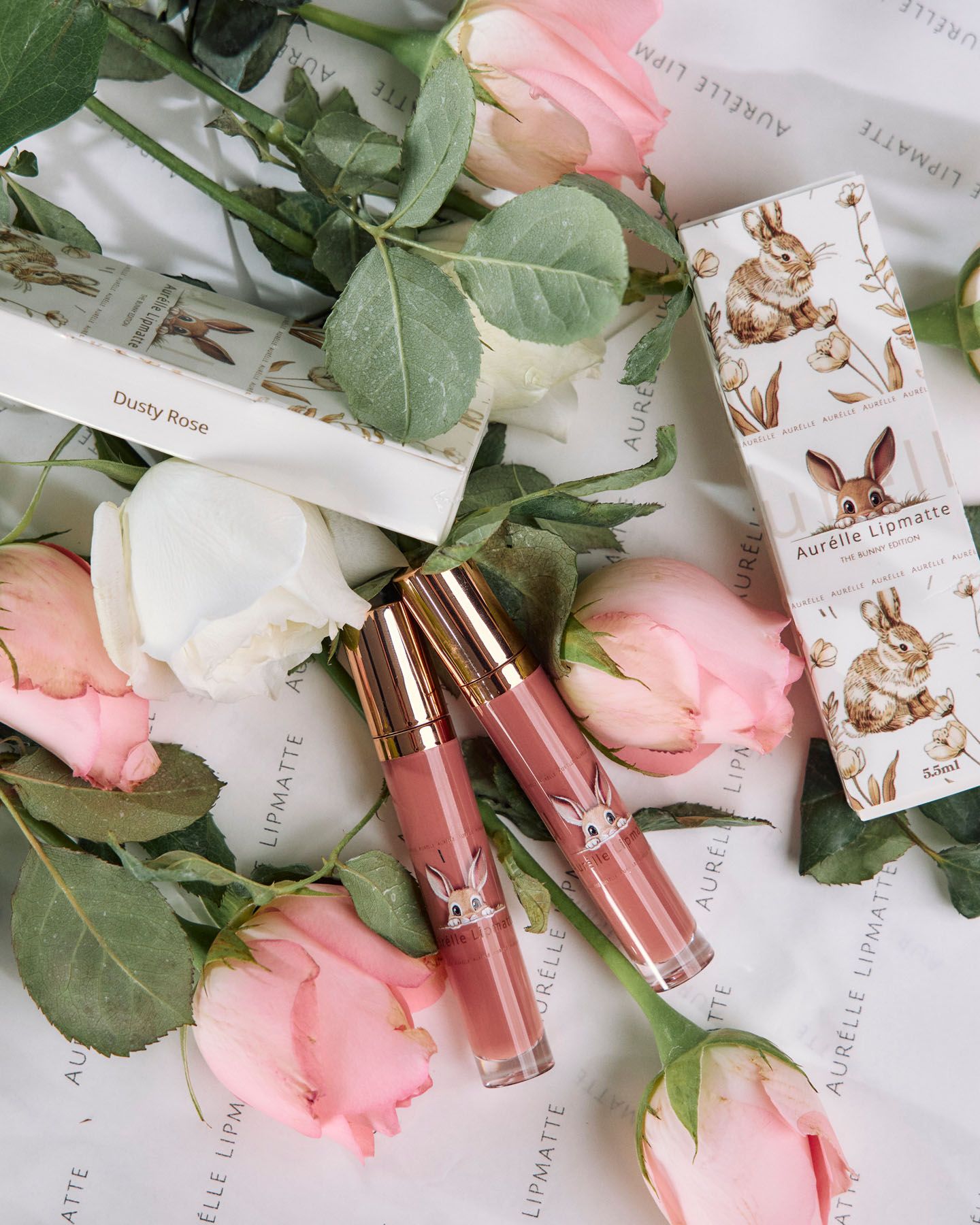 Aurelle Lipmatte in Dusty Rose shade displayed with pink and white roses in elegant product flat lay.