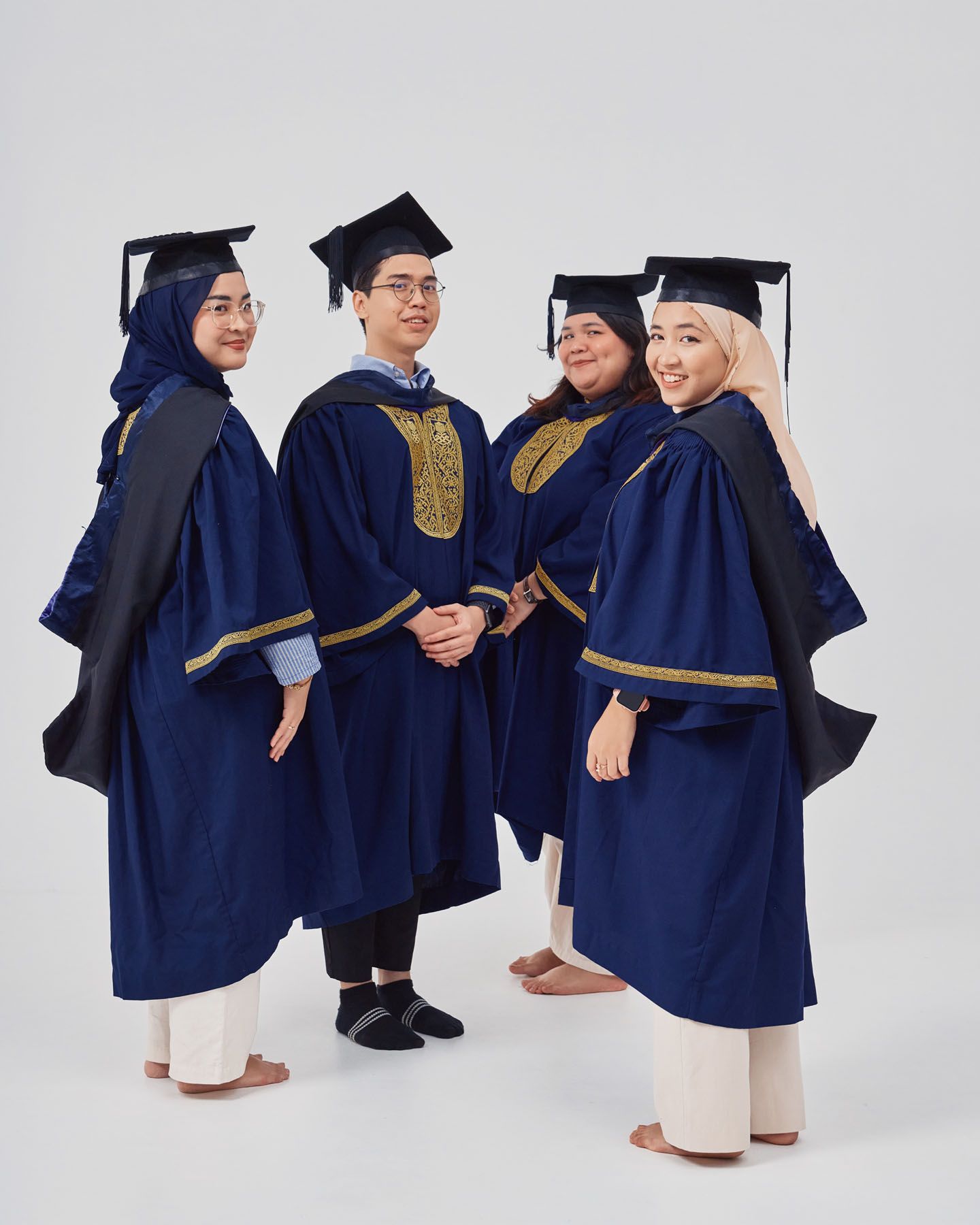 Four graduates in navy academic gowns and caps standing together in a casual graduation photo.