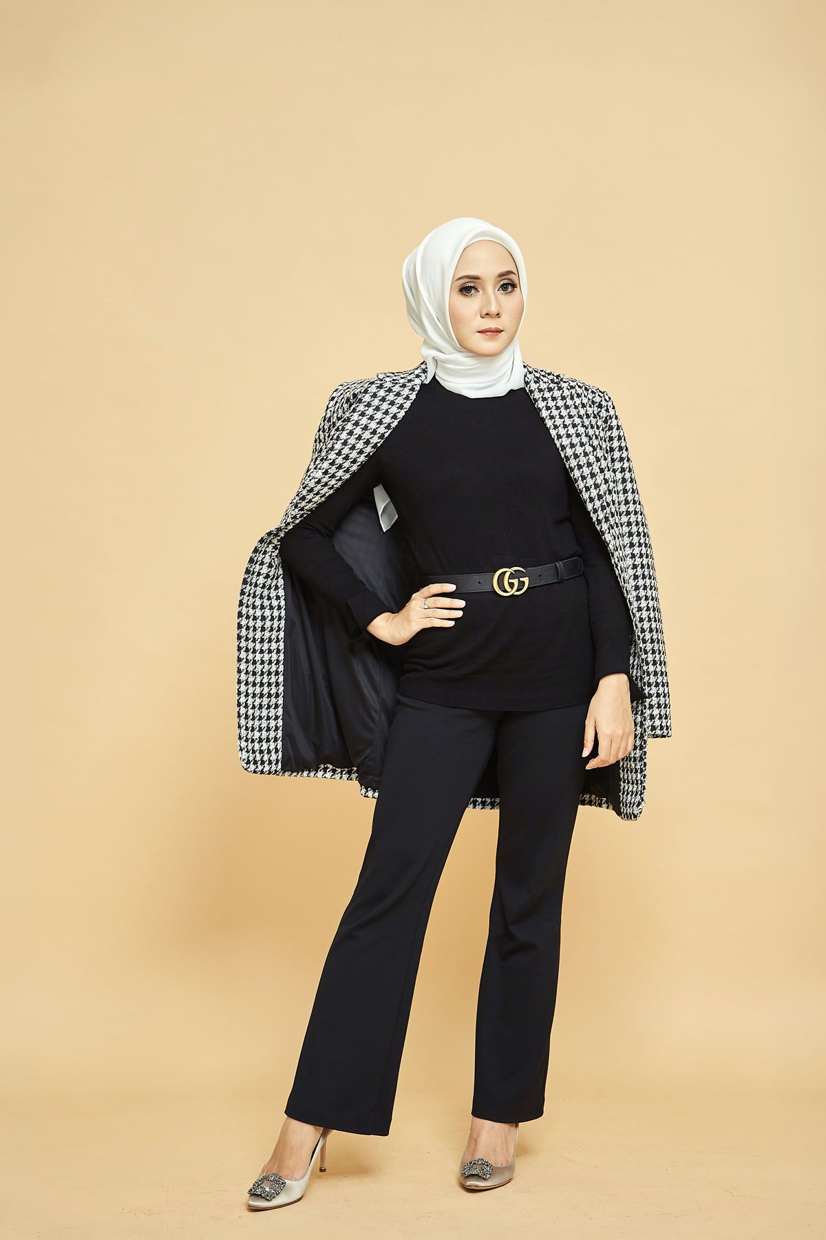 Muslim woman in white hijab with houndstooth blazer draped over shoulders and Gucci belt posing.
