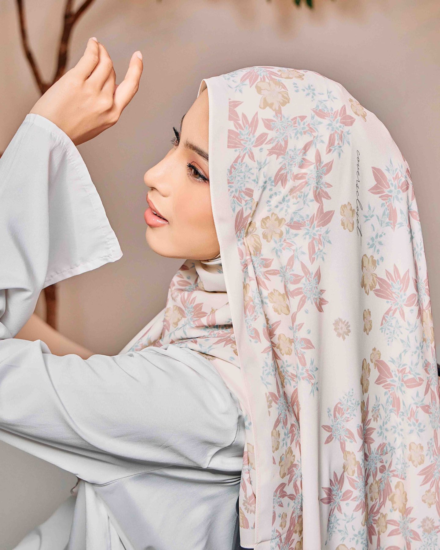 Woman wearing floral printed hijab in soft pink and blue tones with grey long-sleeve outfit.