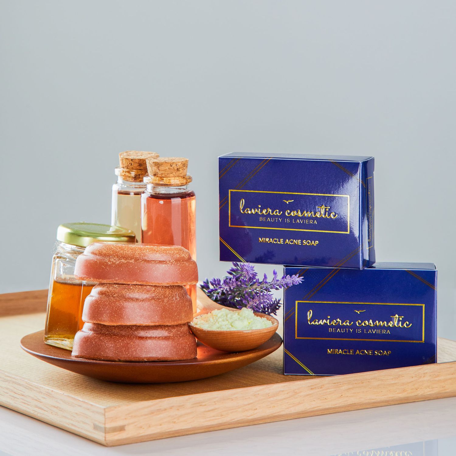 Laviera Cosmetic Miracle Acne Soap bars in navy blue boxes displayed with honey jars and lavender on wooden tray.