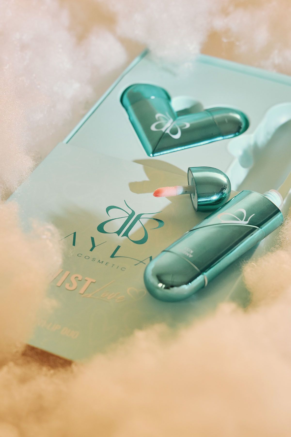 Ayla Cosmetics Twist lip gloss set in teal heart-shaped packaging resting on soft clouds.