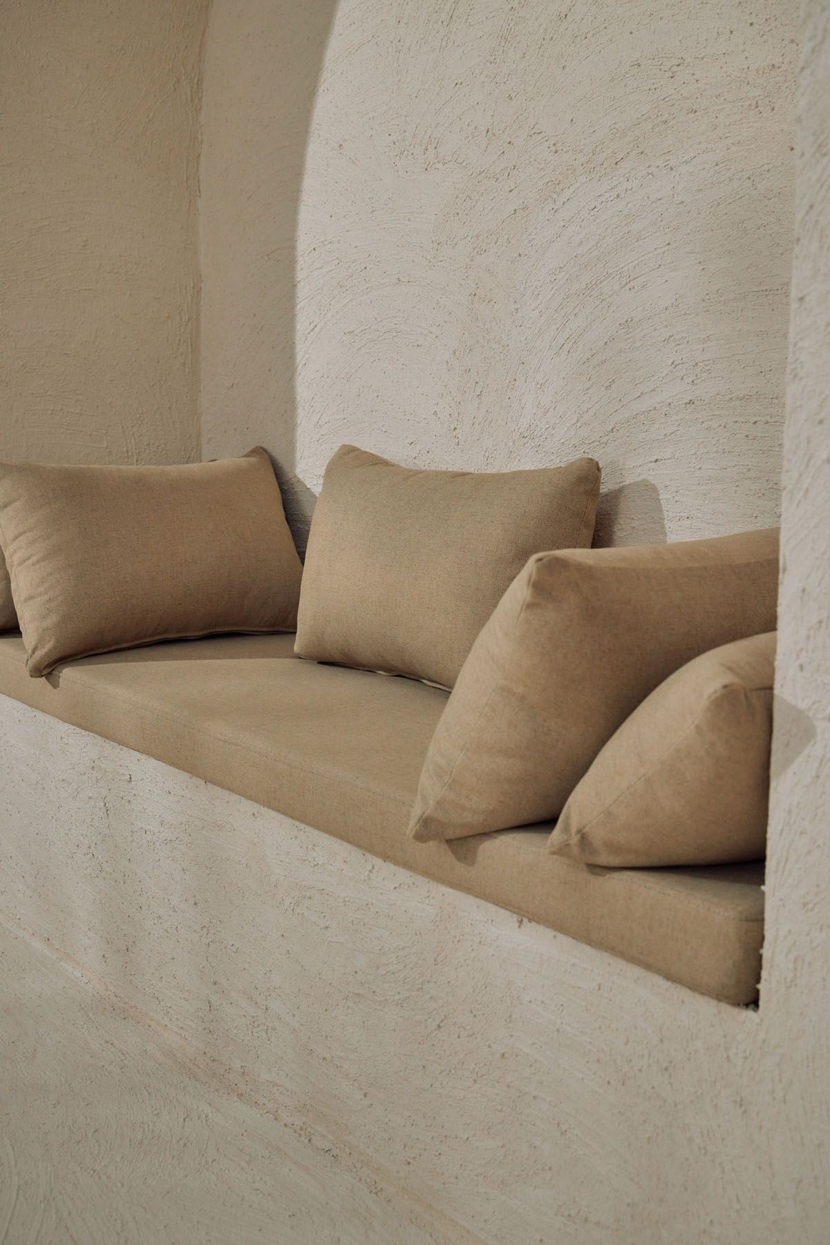Close-up of neutral linen cushions arranged on a built-in plaster bench inside an arched alcove.