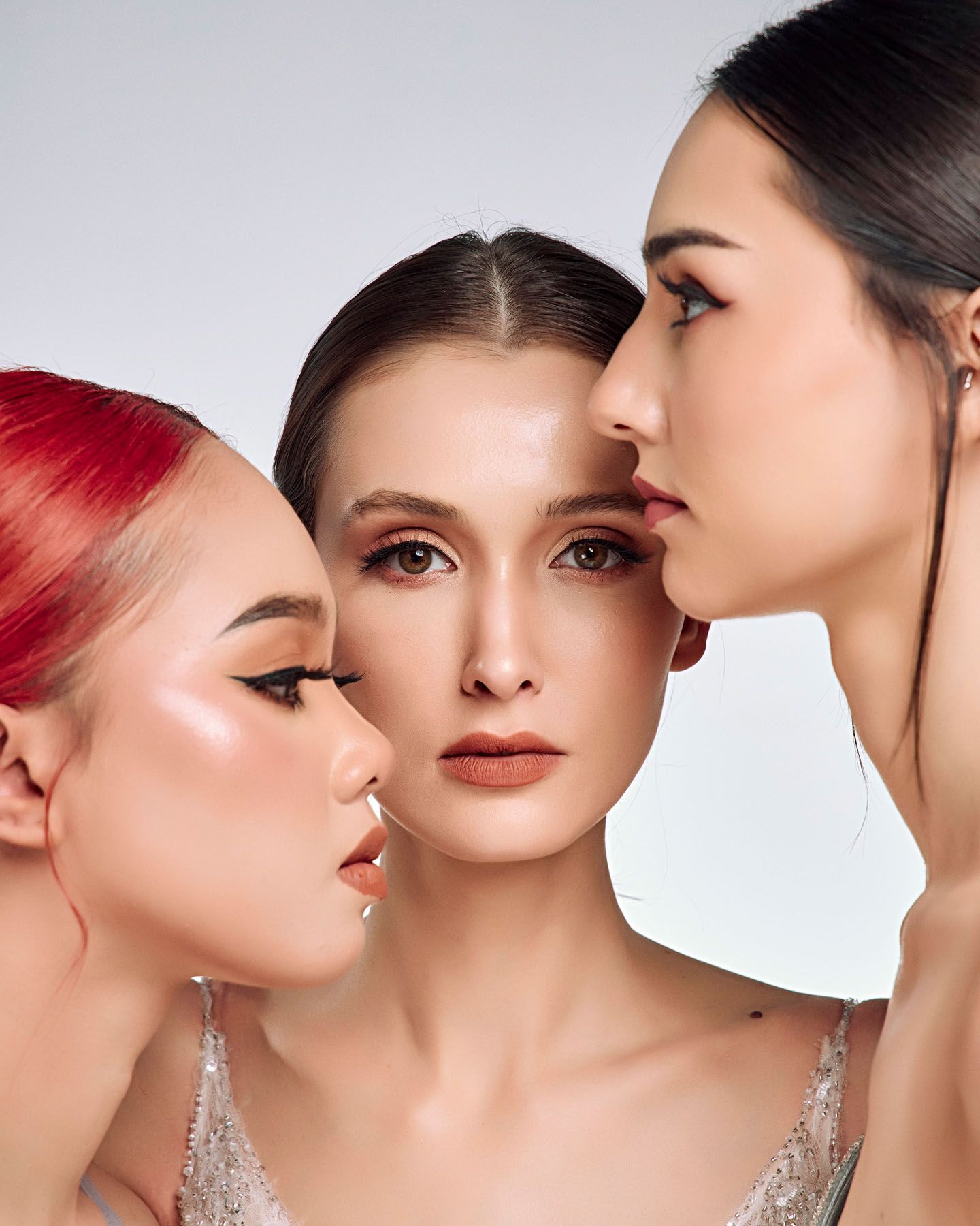 Three models with dramatic makeup pose closely together in a stunning beauty editorial shoot.