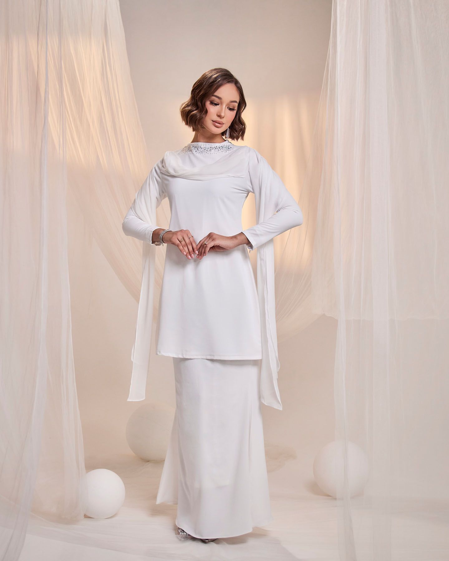 Woman in elegant white long-sleeve modest dress with flowing sleeve details and matching skirt.