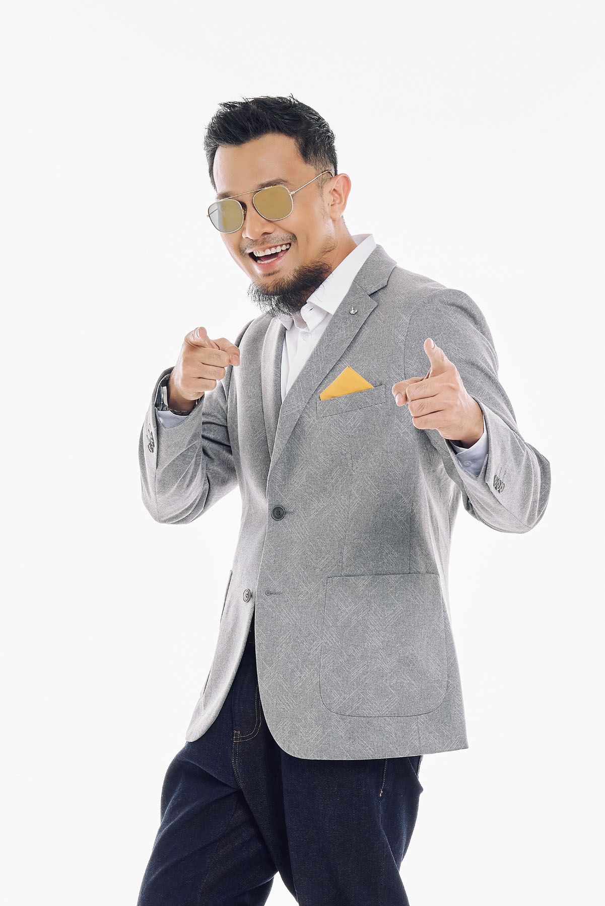 Cheerful Asian man in gray blazer and gold sunglasses pointing finger guns at camera.