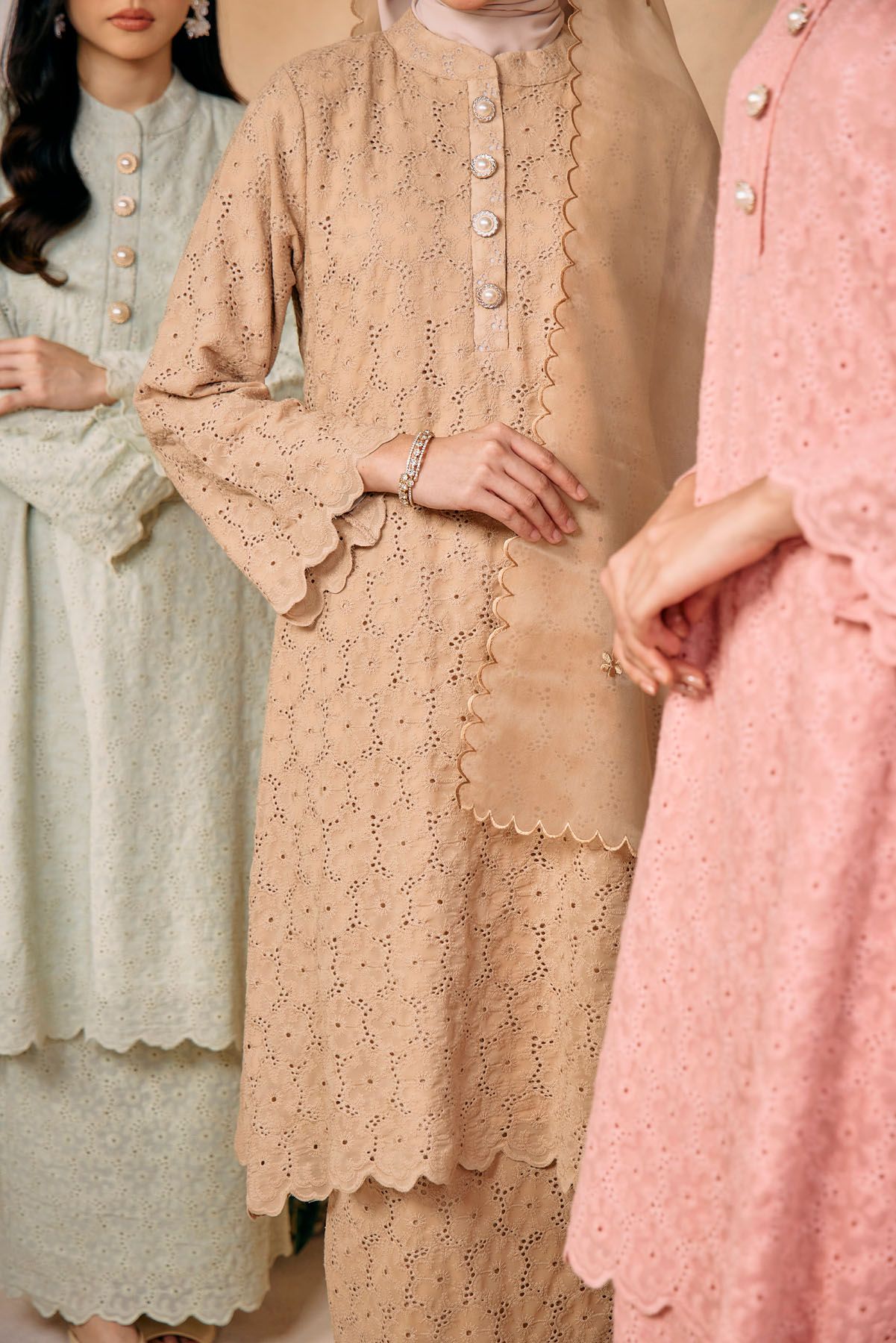 Close-up of three women wearing broderie anglaise baju kurung in beige, mint, and pink tones.