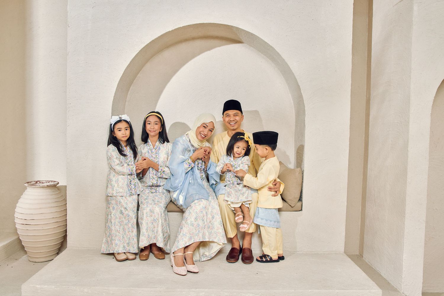 Muslim family in blue and white traditional baju kurung and baju melayu posing together for Eid celebration photo.