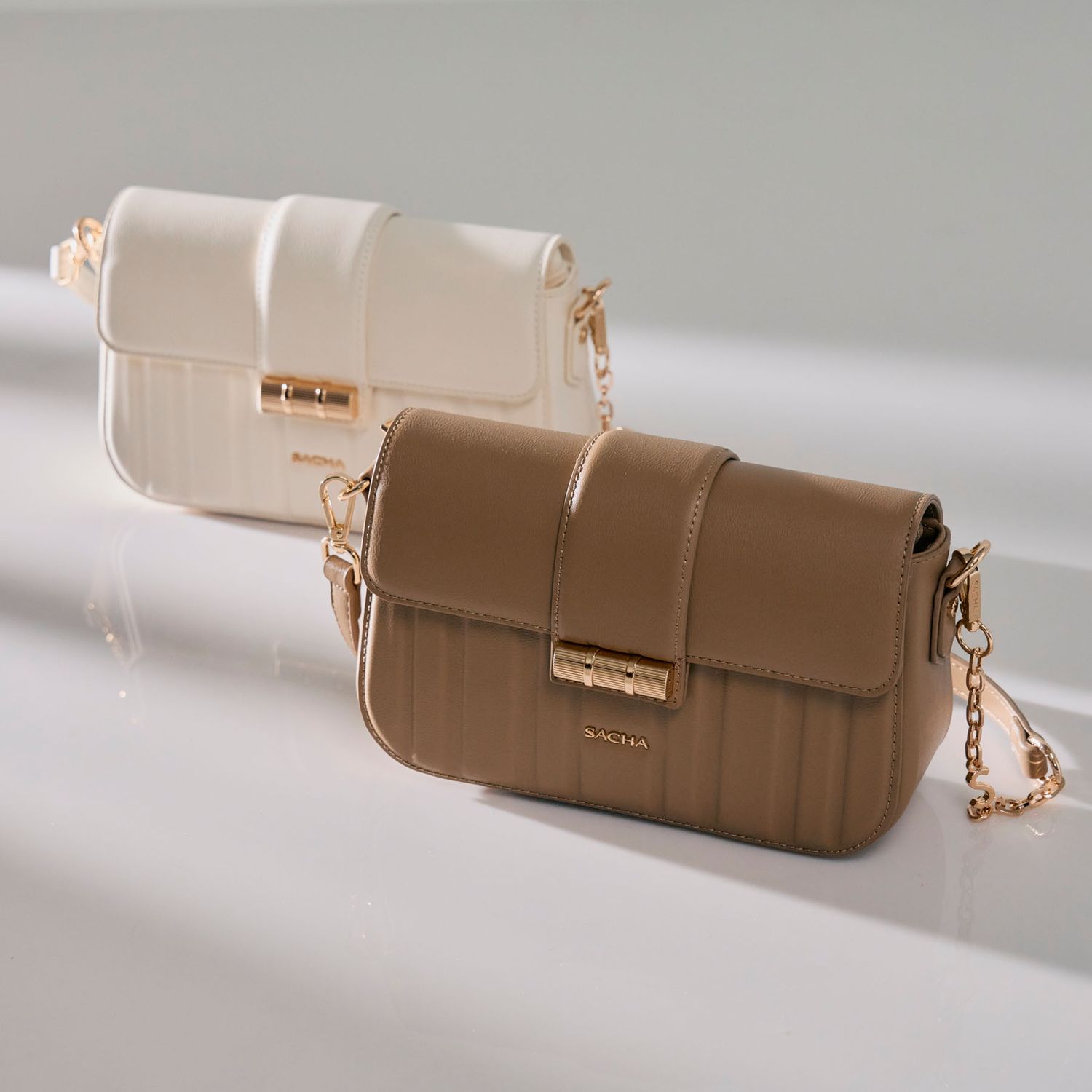 Two quilted leather crossbody bags in cream and brown with gold chain straps on a reflective surface.