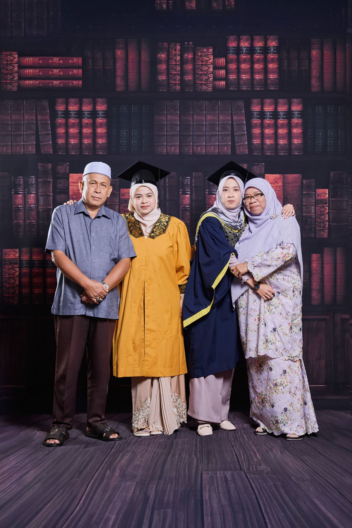 Muslim family graduation photo with two daughters in caps and gowns posing with proud parents.