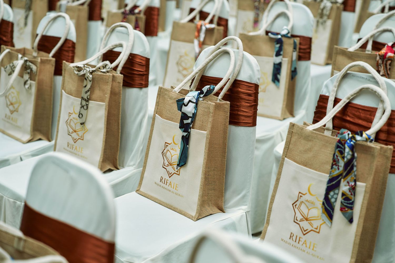 Rows of branded burlap gift bags with red handles and decorative scarves at event venue.