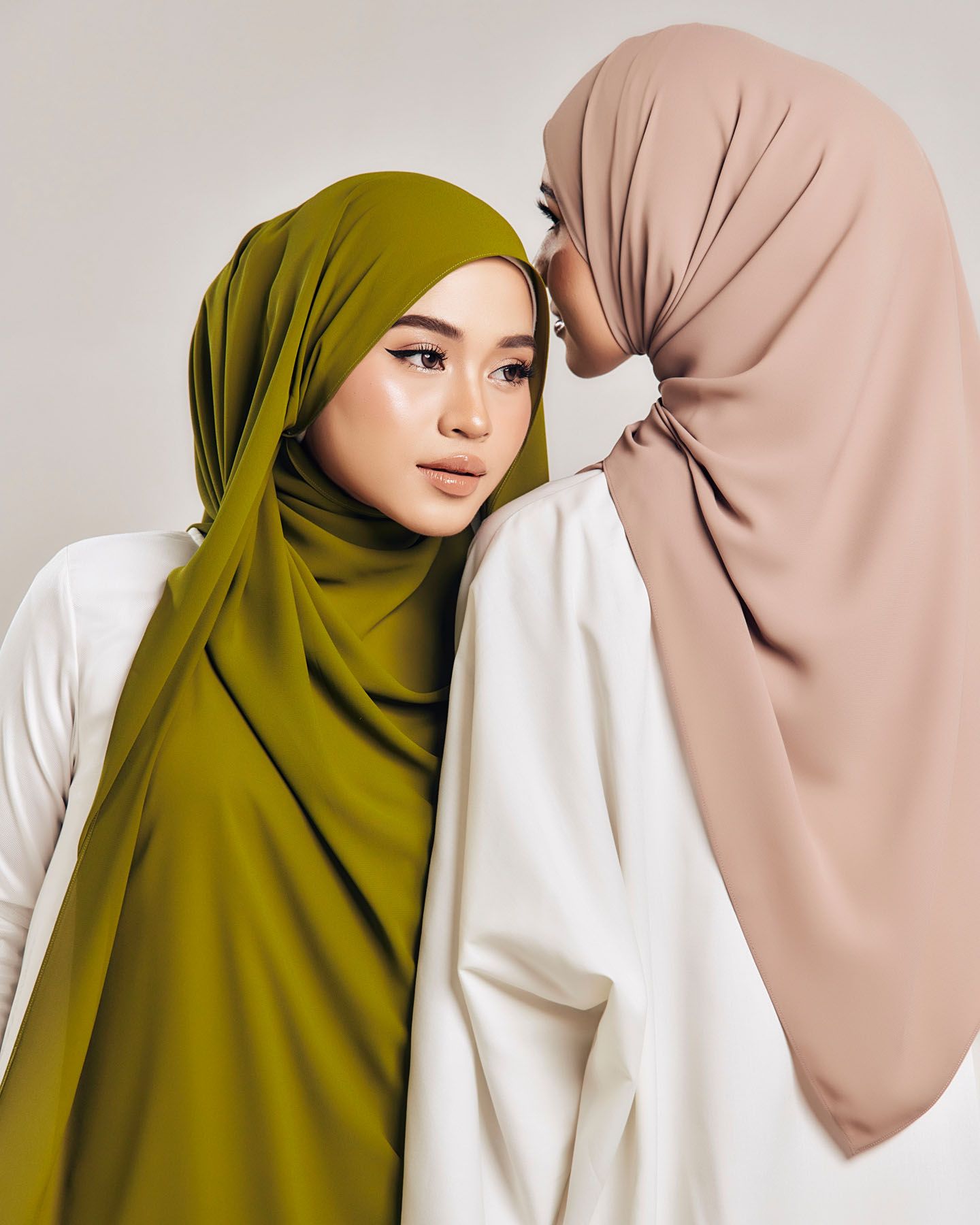 Two women model elegant hijabs in olive green and nude pink tones against a neutral background.