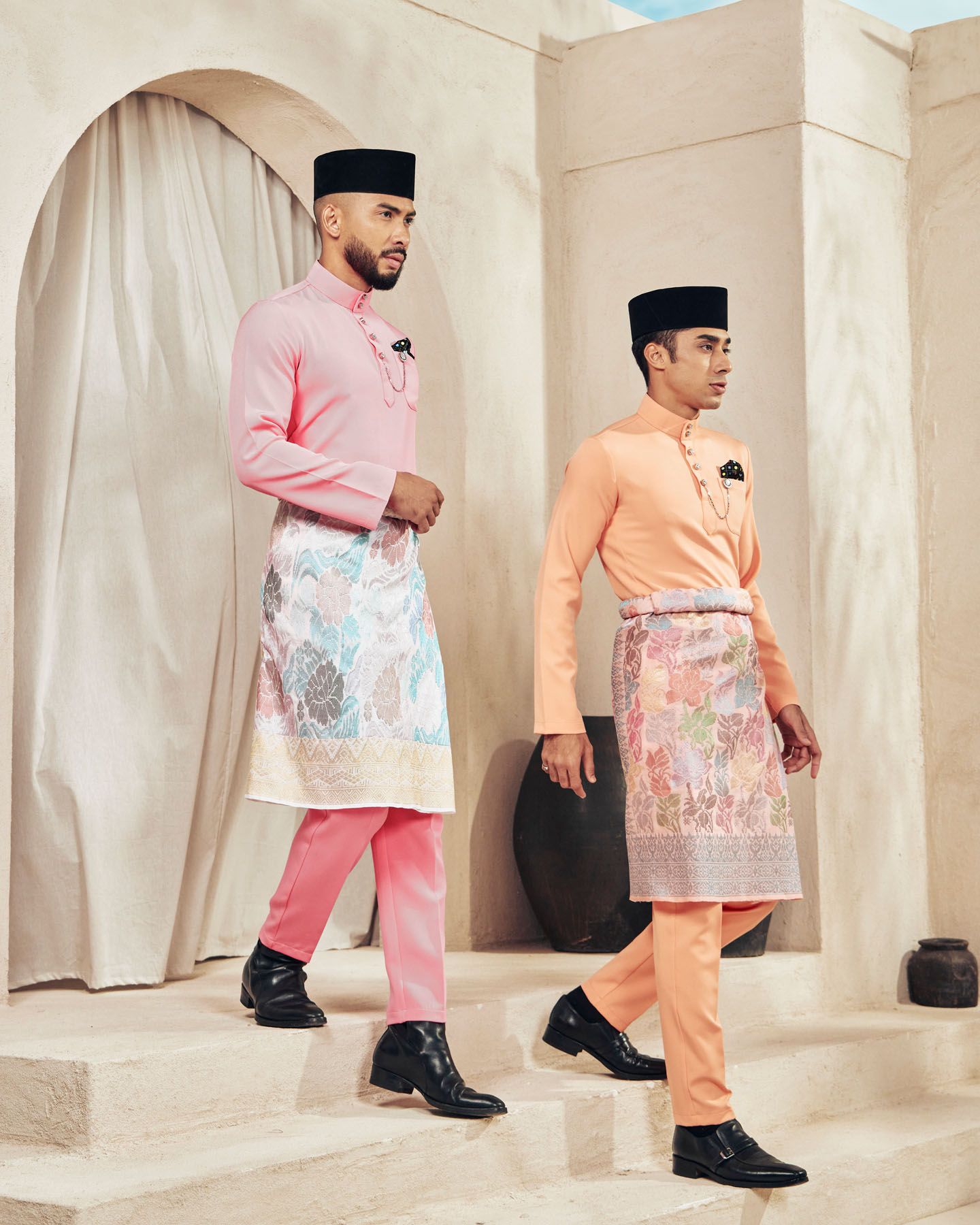 Two men in pink and peach baju melayu with floral sampin walk on steps.