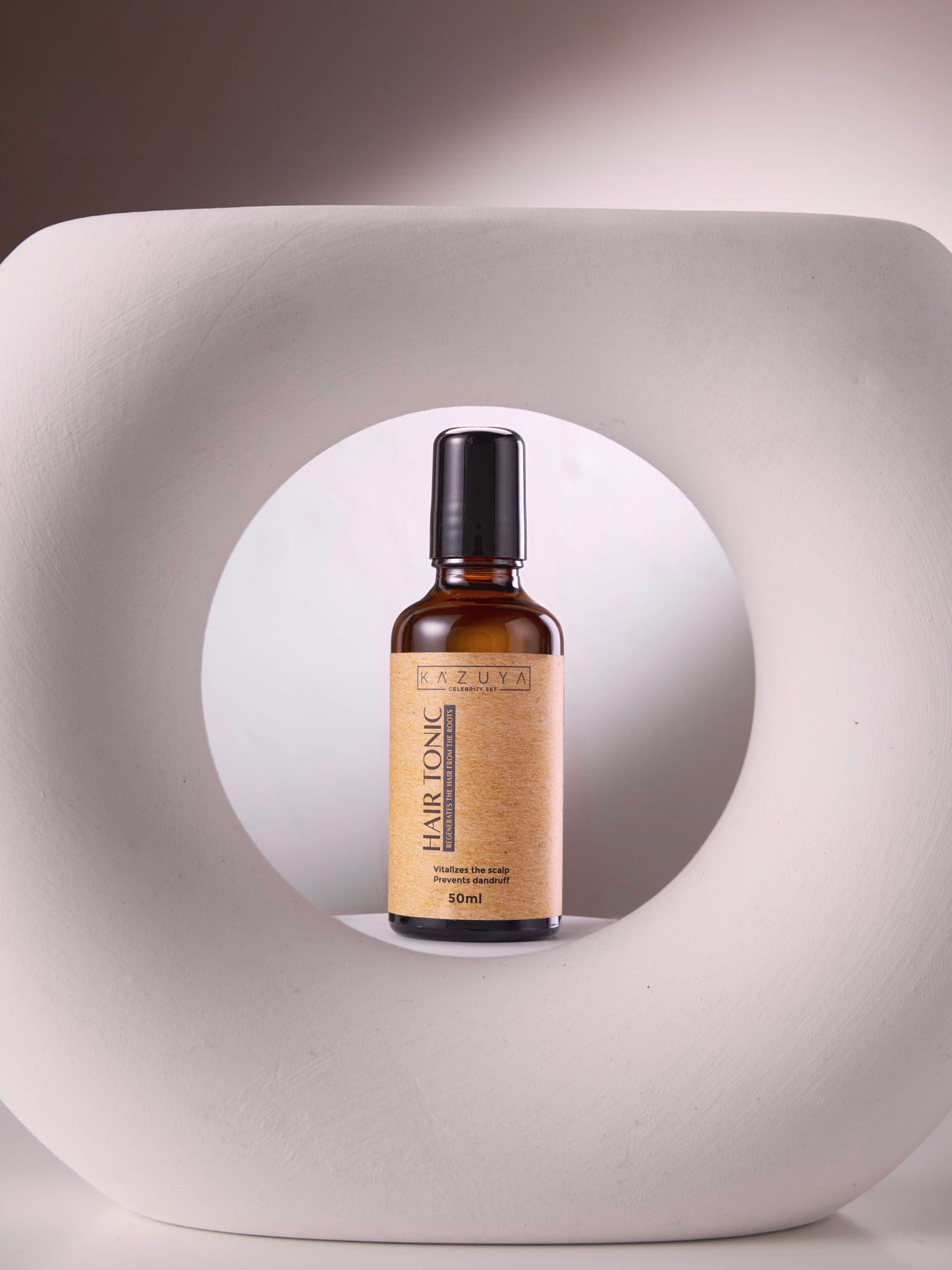 KAZUYA Hair Tonic 60ml amber glass dropper bottle displayed in circular white sculptural prop.