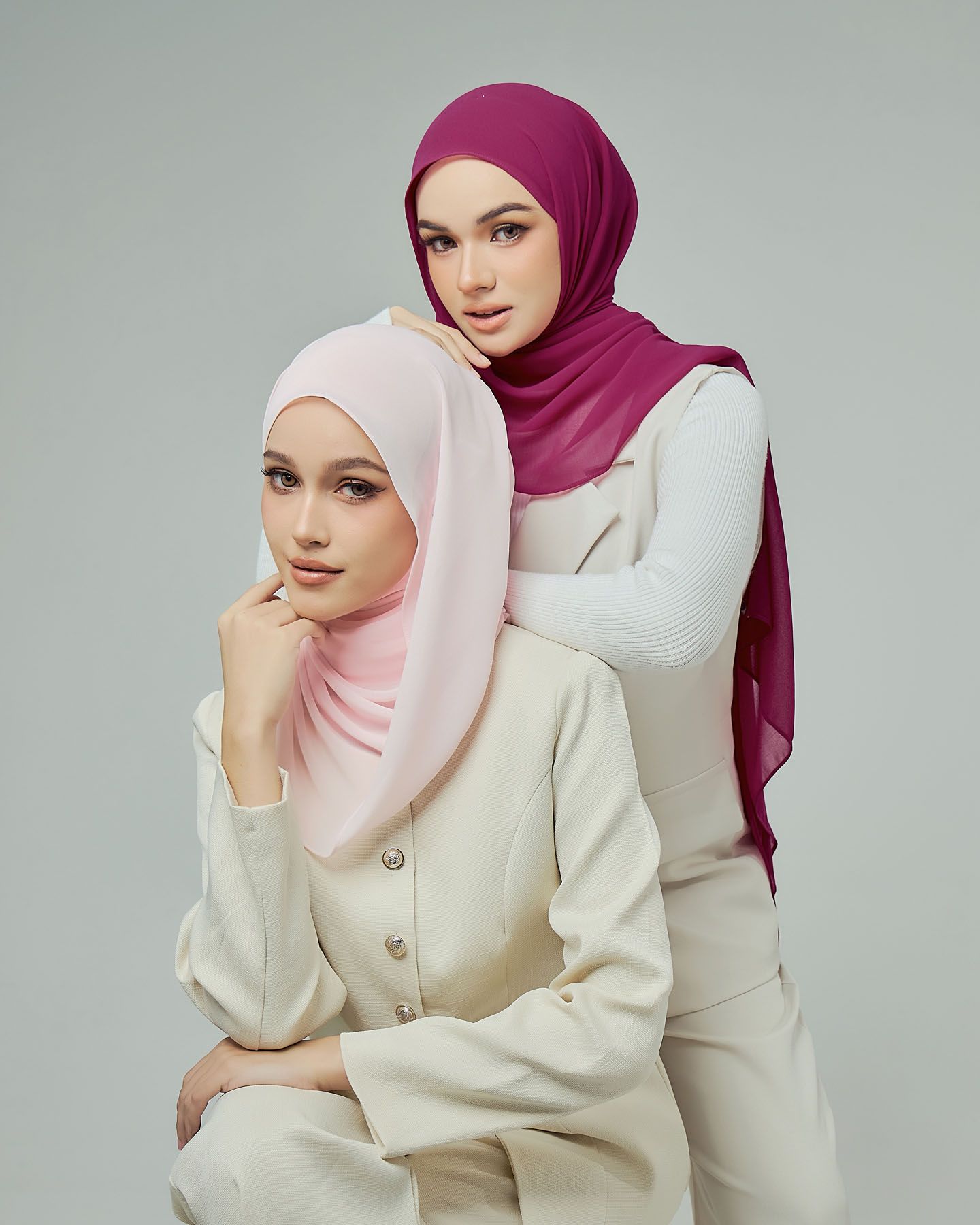 Two women wearing pink and magenta chiffon hijabs with cream blazers in studio fashion shoot.