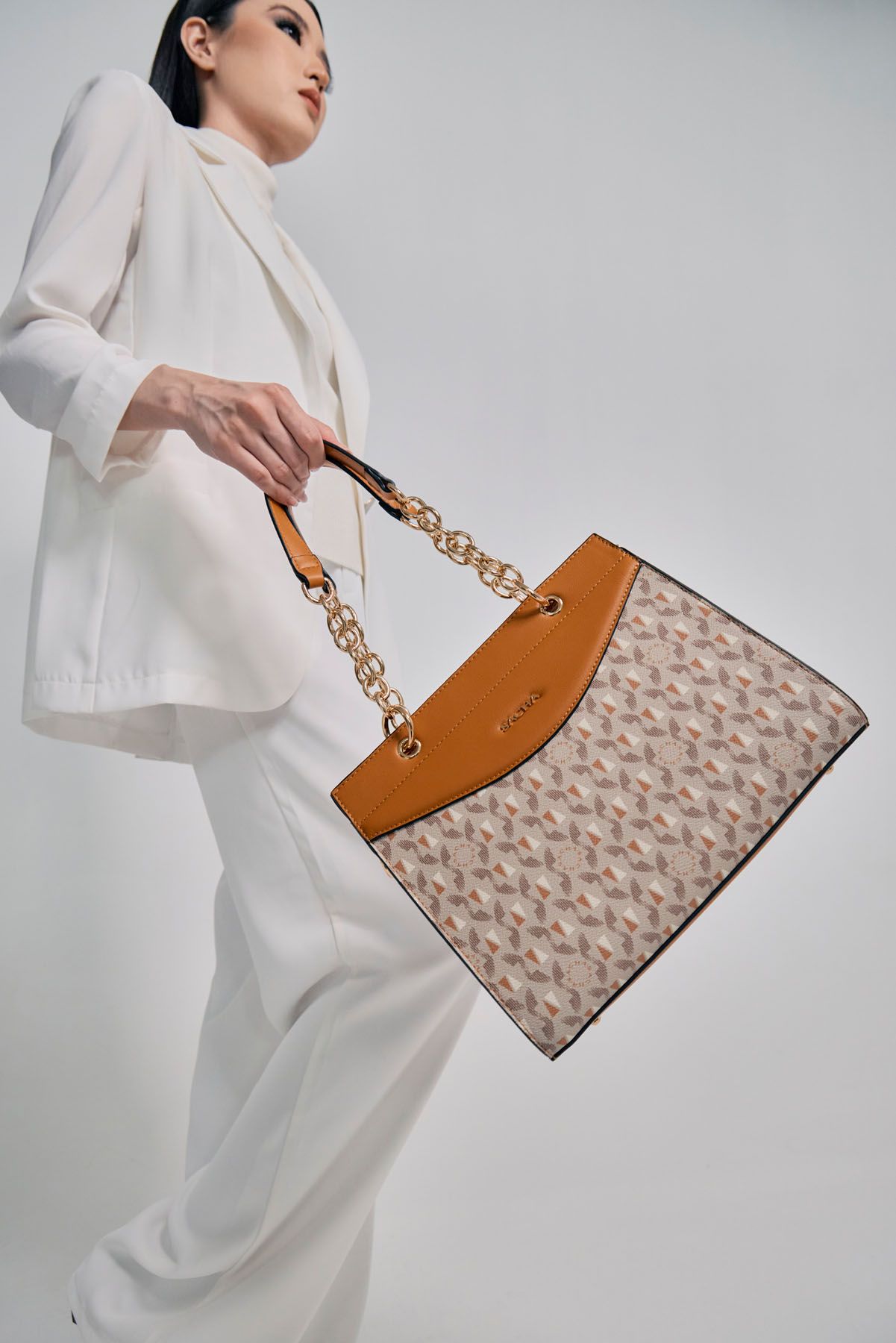 Woman in white suit carrying large patterned tote bag with gold chain handles.
