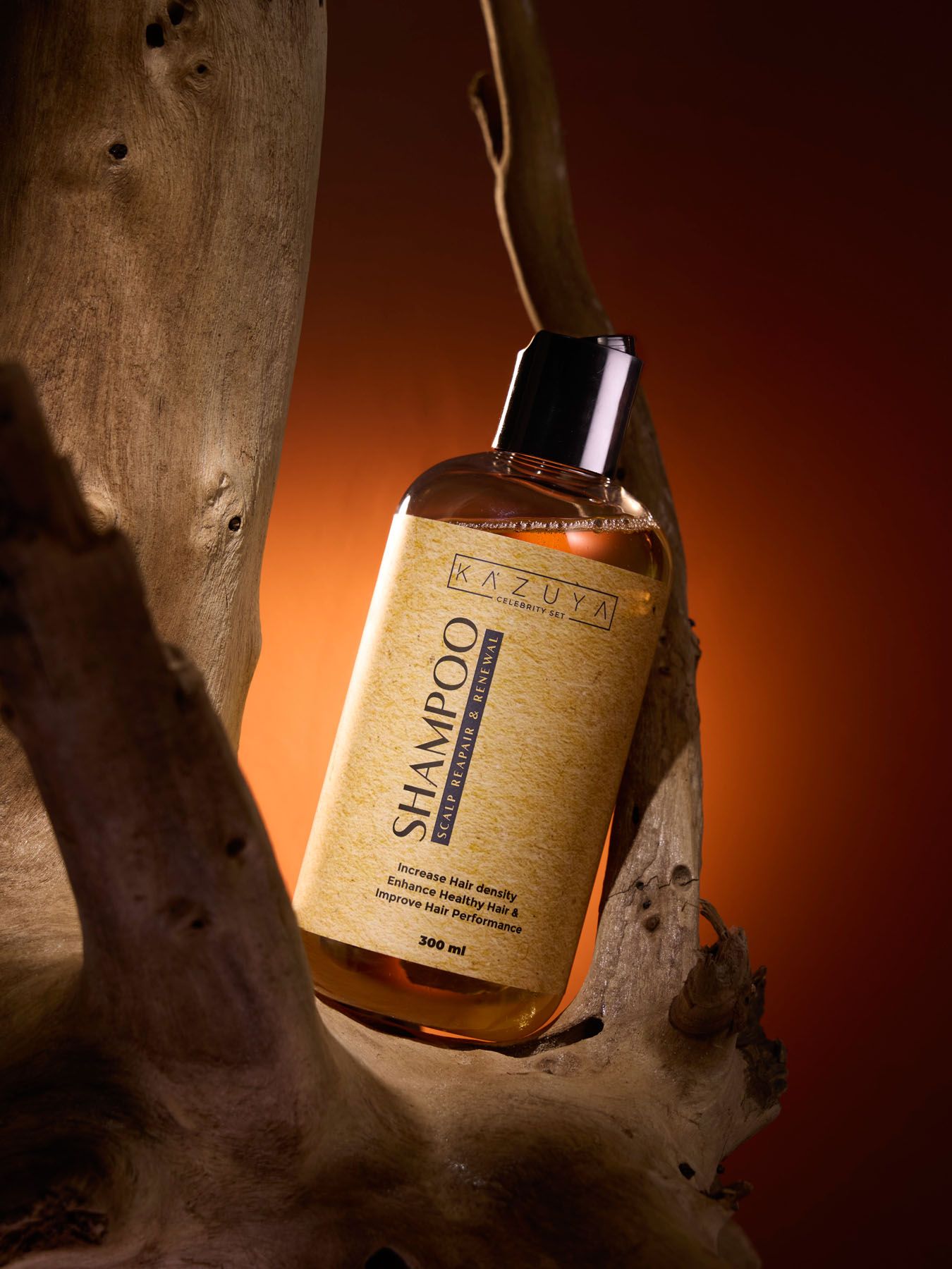 Kazuya shampoo bottle with golden label suspended against driftwood with a warm orange background.