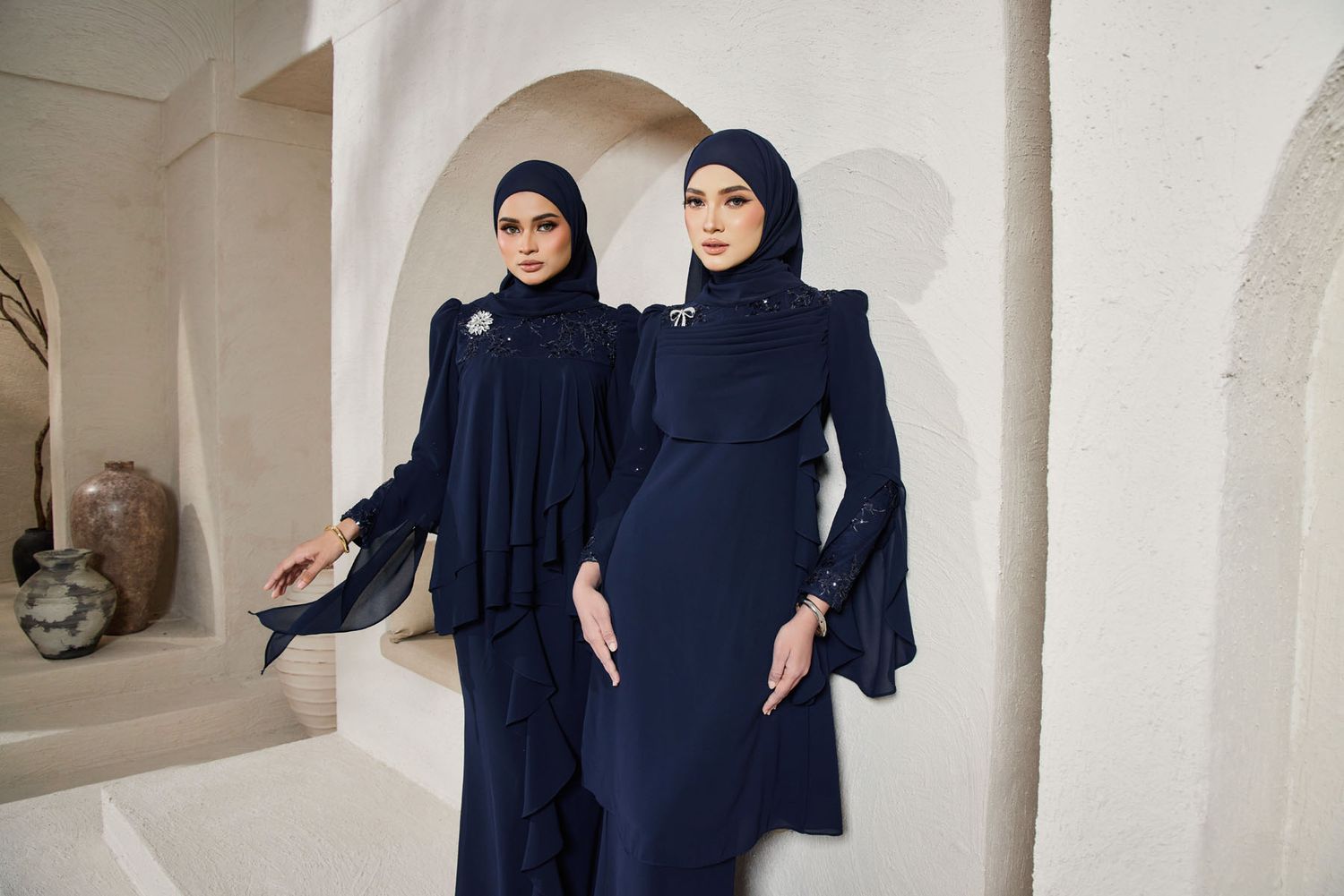 Two women in navy blue modest fashion baju kurung with dramatic sleeves and matching hijabs.