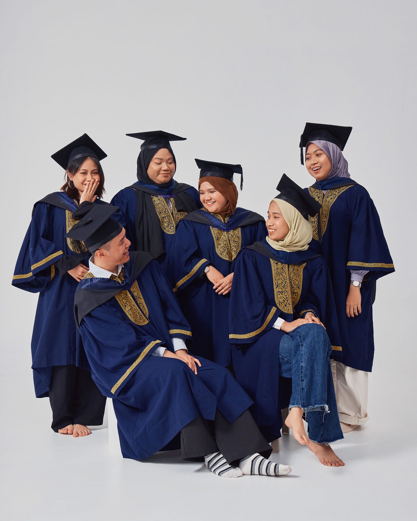 Group of six graduates in navy and gold robes laughing and posing together for graduation photo.