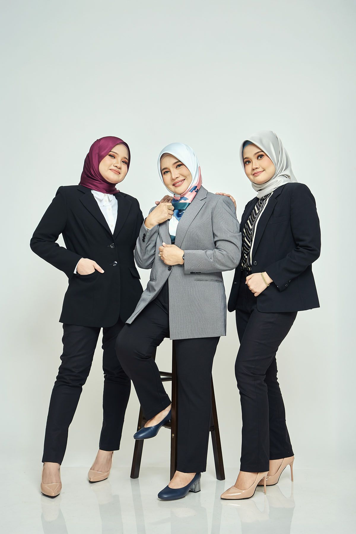 Three Muslim businesswomen in hijabs and blazers posing confidently in a professional studio setting.