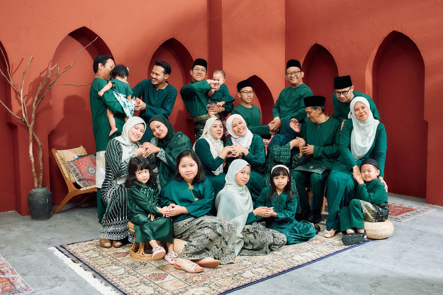 Large family group in coordinating green Hari Raya outfits posing together in a terracotta courtyard.
