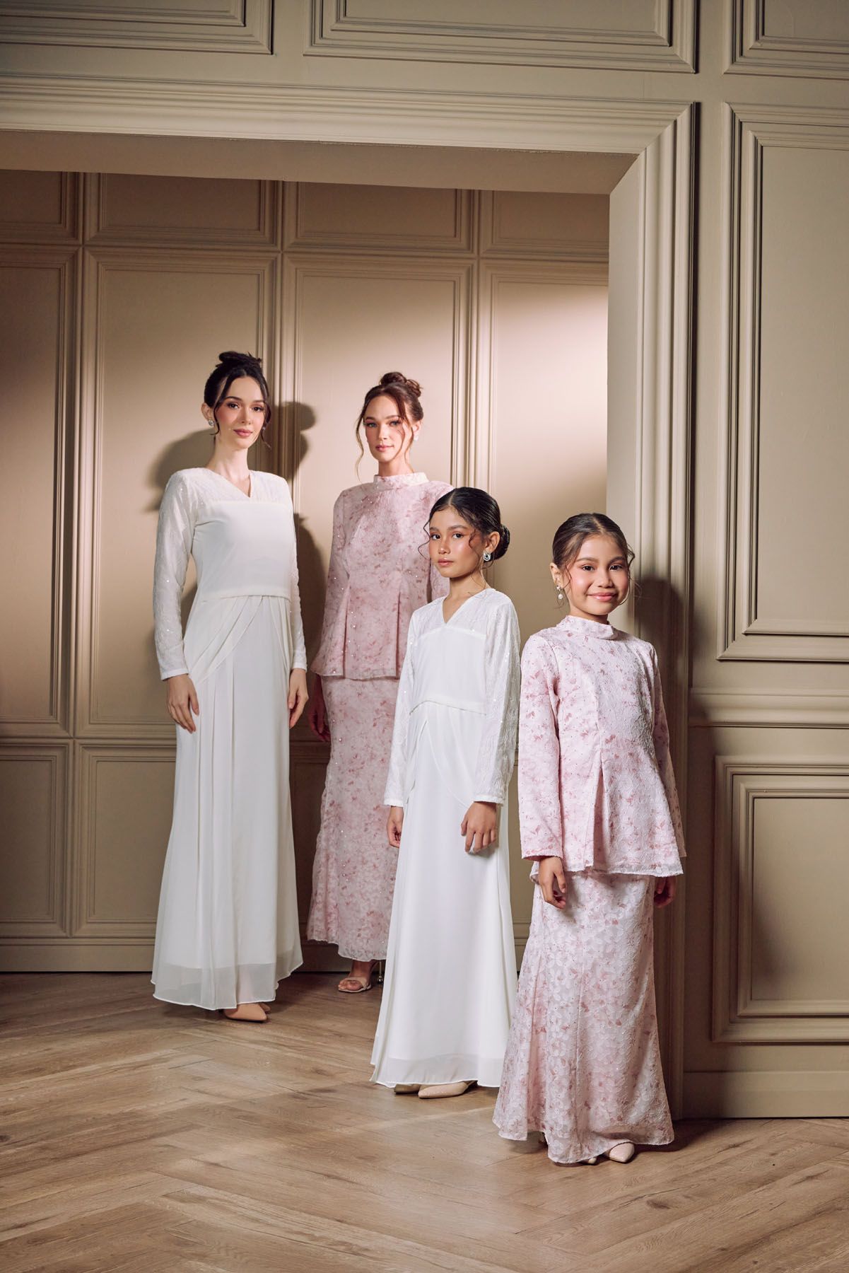 Four women and girls in white and pink baju kurung pose in elegant room.