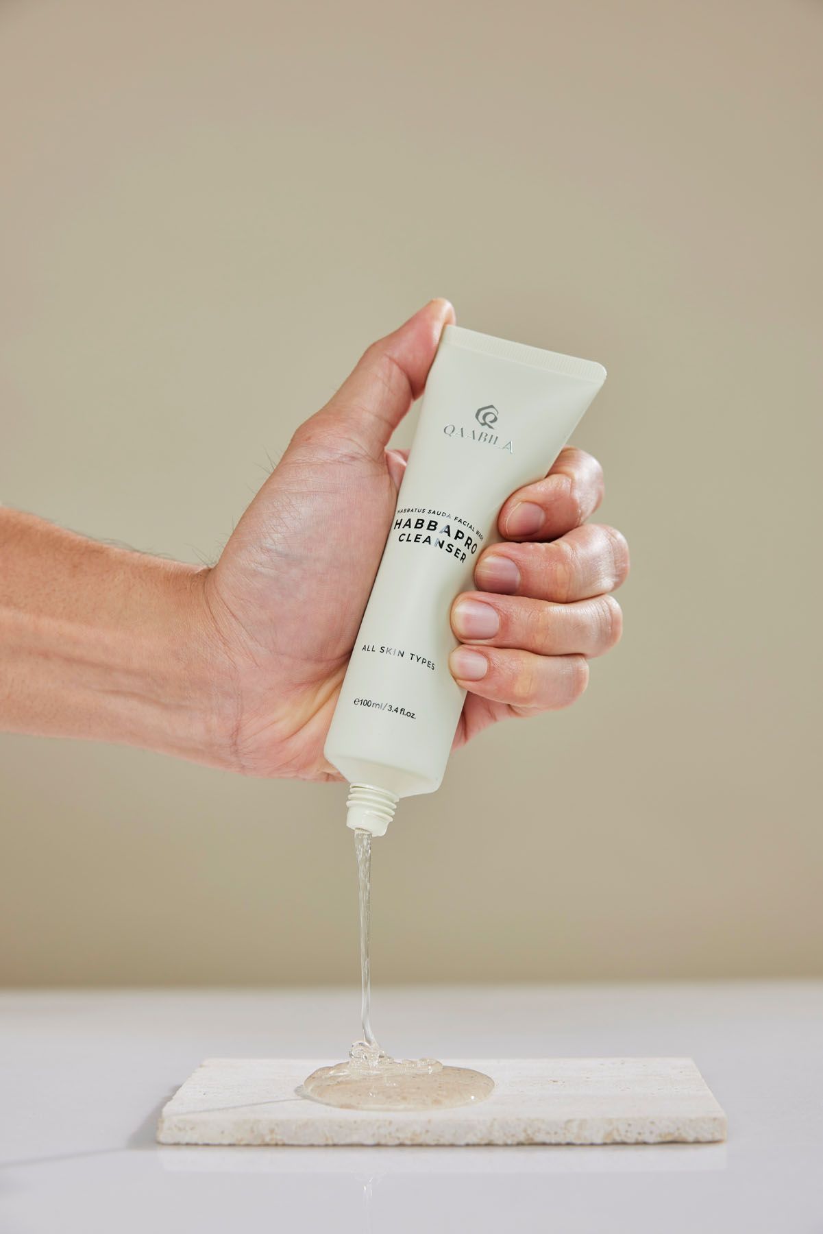 Hand squeezing clear gel from O'Clarice Garbage Cleanser tube onto white marble surface against neutral background.