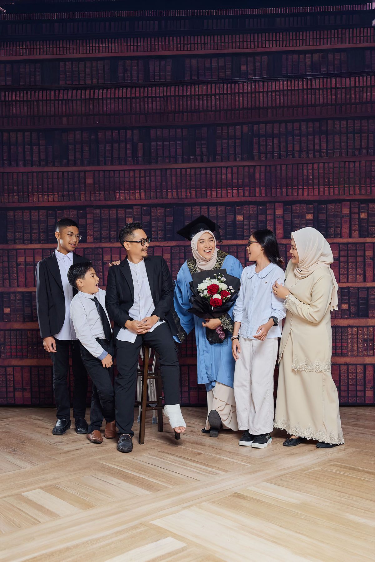 Muslim family celebrating graduation with woman in blue cap and gown holding bouquet.