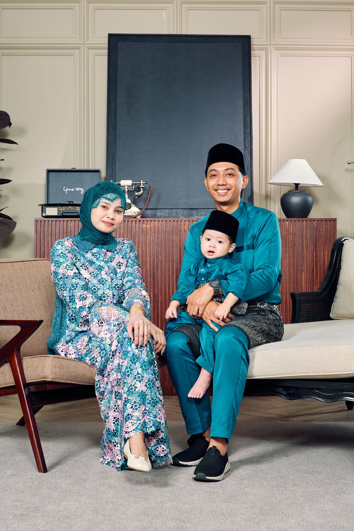 Malaysian family in matching teal Baju Melayu and Baju Kurung outfits posing for Hari Raya portrait with baby.
