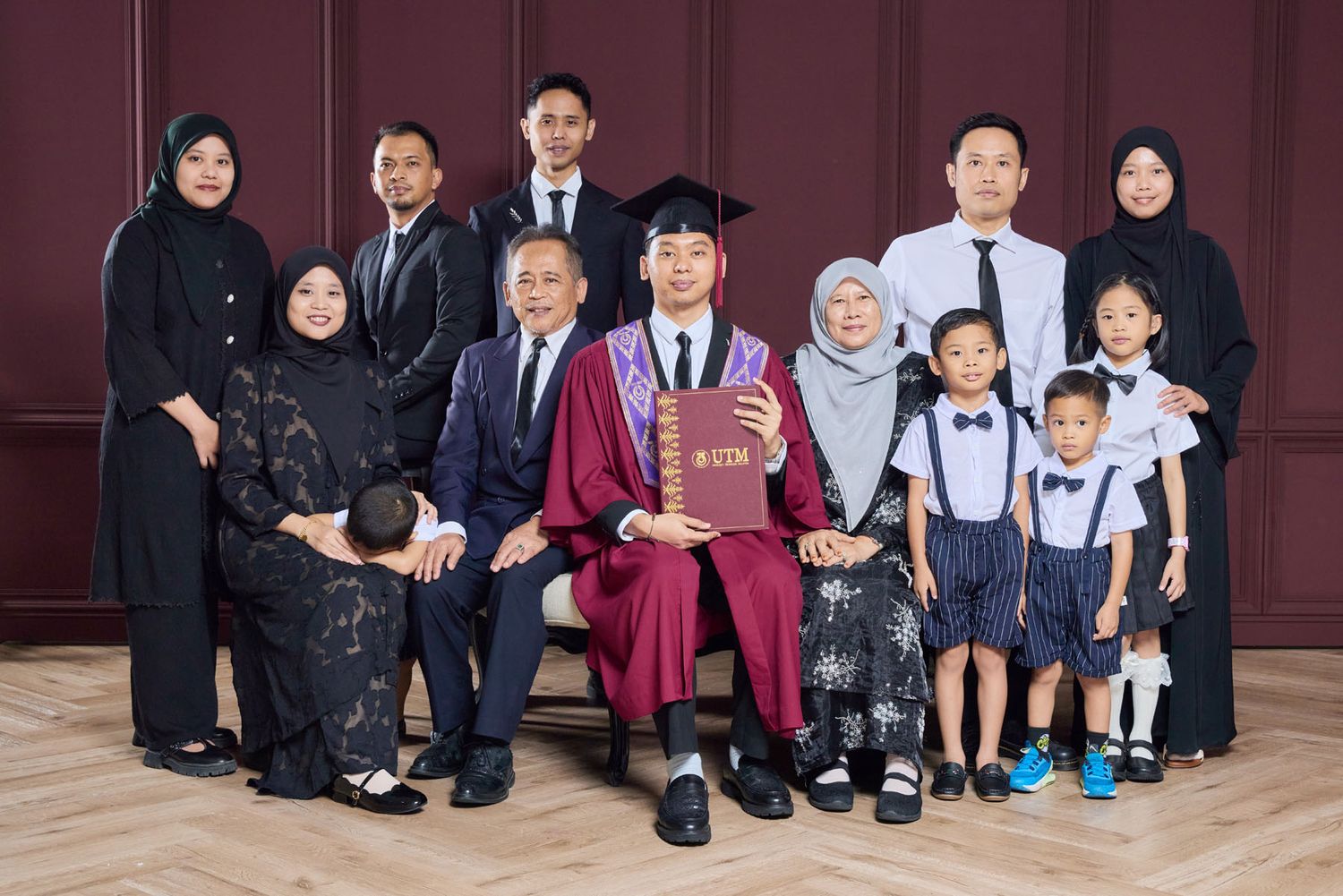 Family graduation portrait with graduate in maroon UTM regalia seated among relatives in studio.