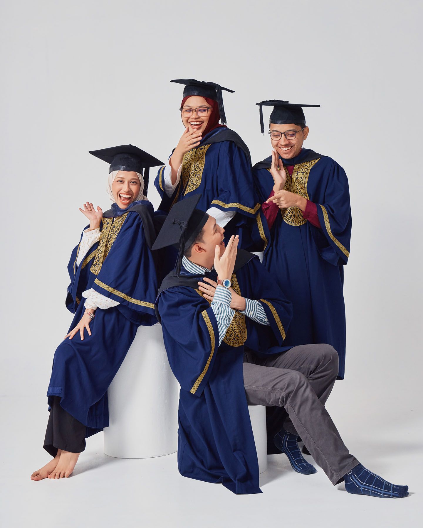 Four graduates in navy robes laughing and posing playfully for graduation photos.