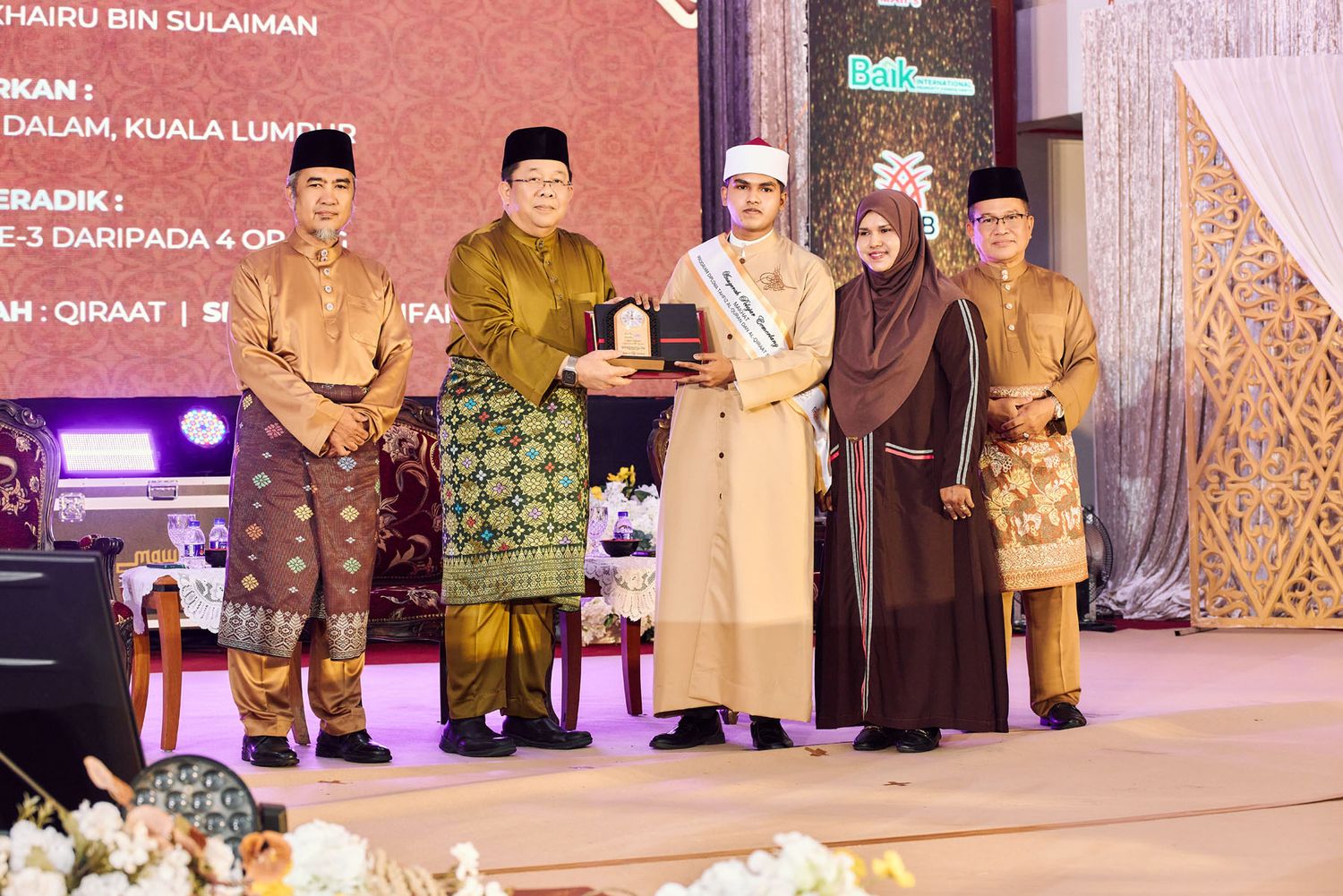 Award presentation ceremony with recipients in traditional Malaysian attire receiving recognition at a Quran event.