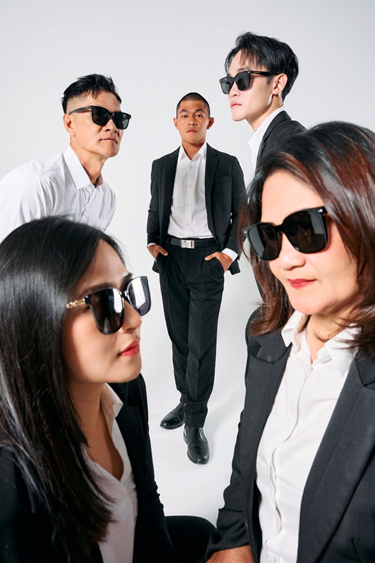 Five professionals in black suits and sunglasses pose together in a stylish group photo against a white background.