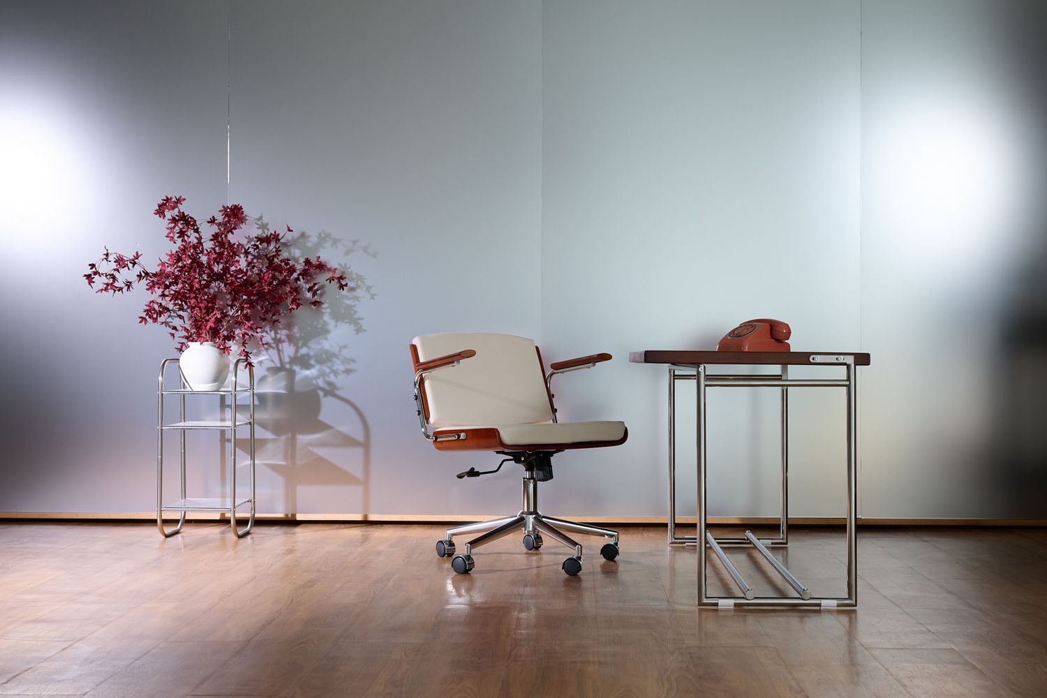 Modern office chair with wooden armrests on casters beside a sleek side table and red floral arrangement in a minimalist room.