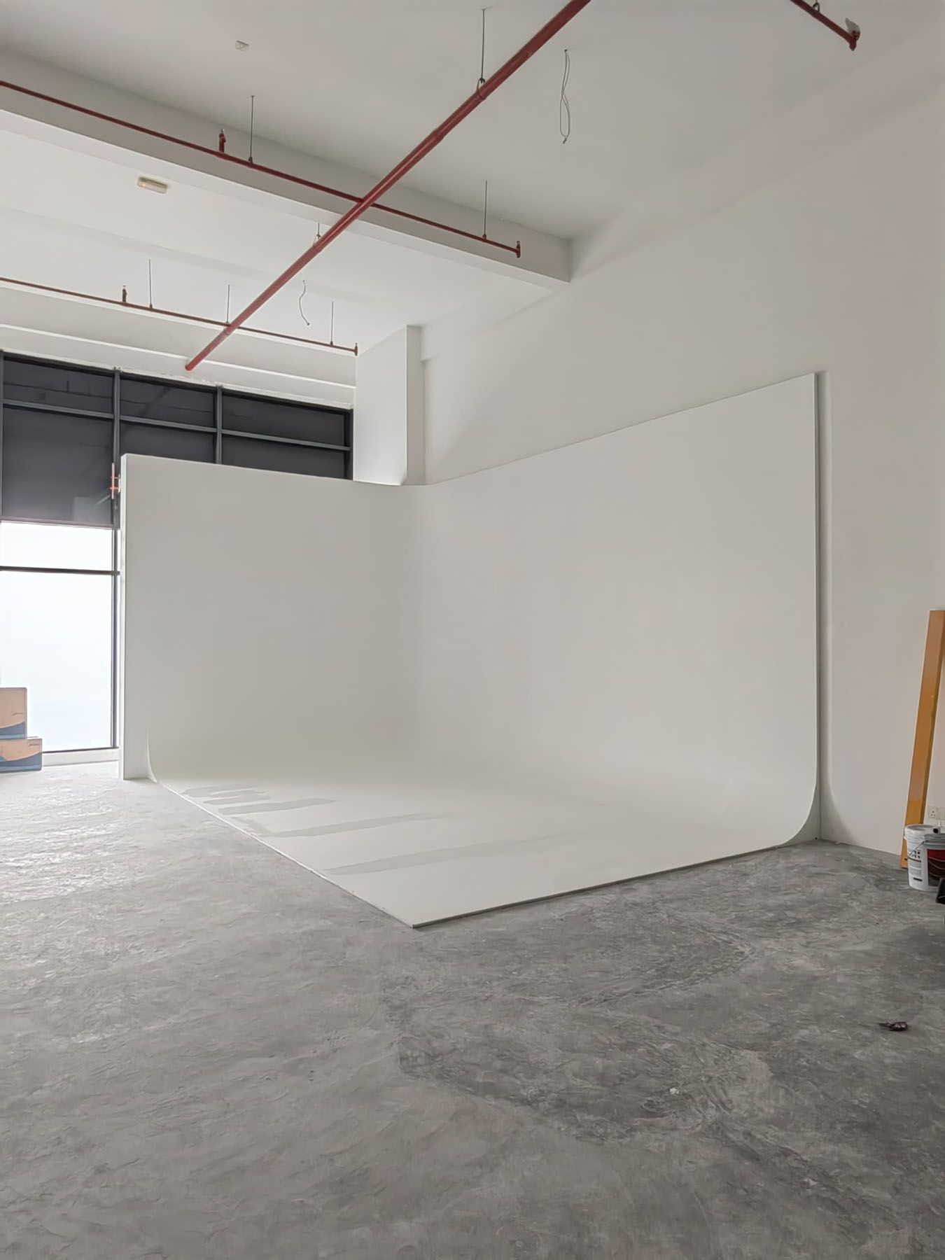 Wide angle view of a white seamless photography backdrop in a spacious studio with high ceilings.