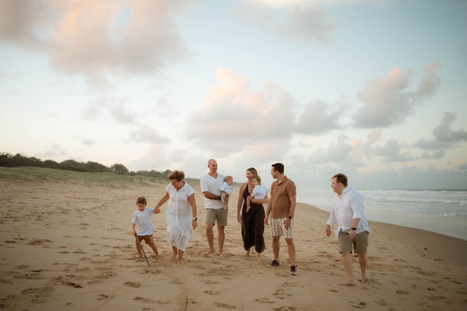 Happy family walking together on sandy beach under pastel cloudy sky.