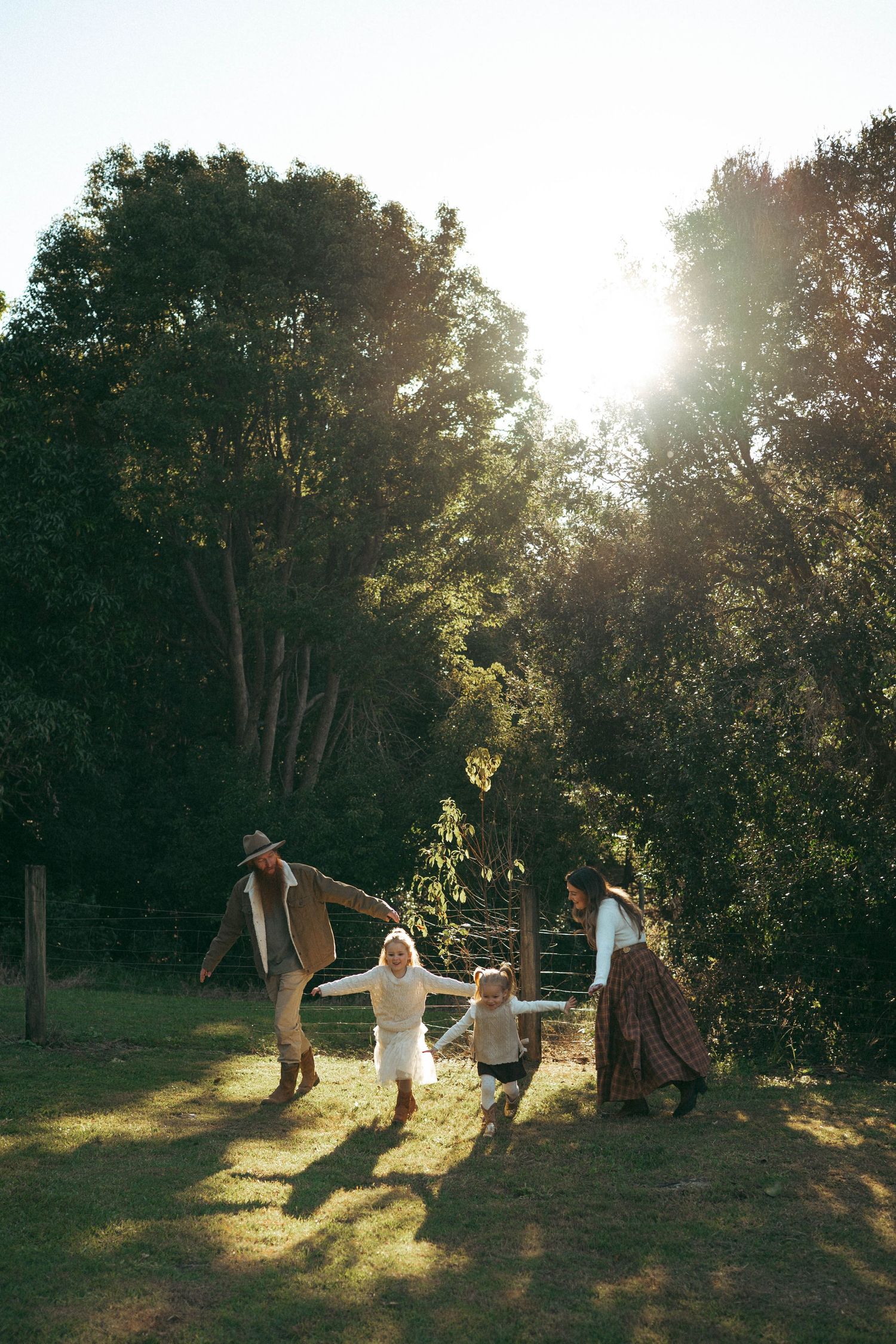 Family playing outdoors in golden sunlight among lush green trees on a grassy lawn.