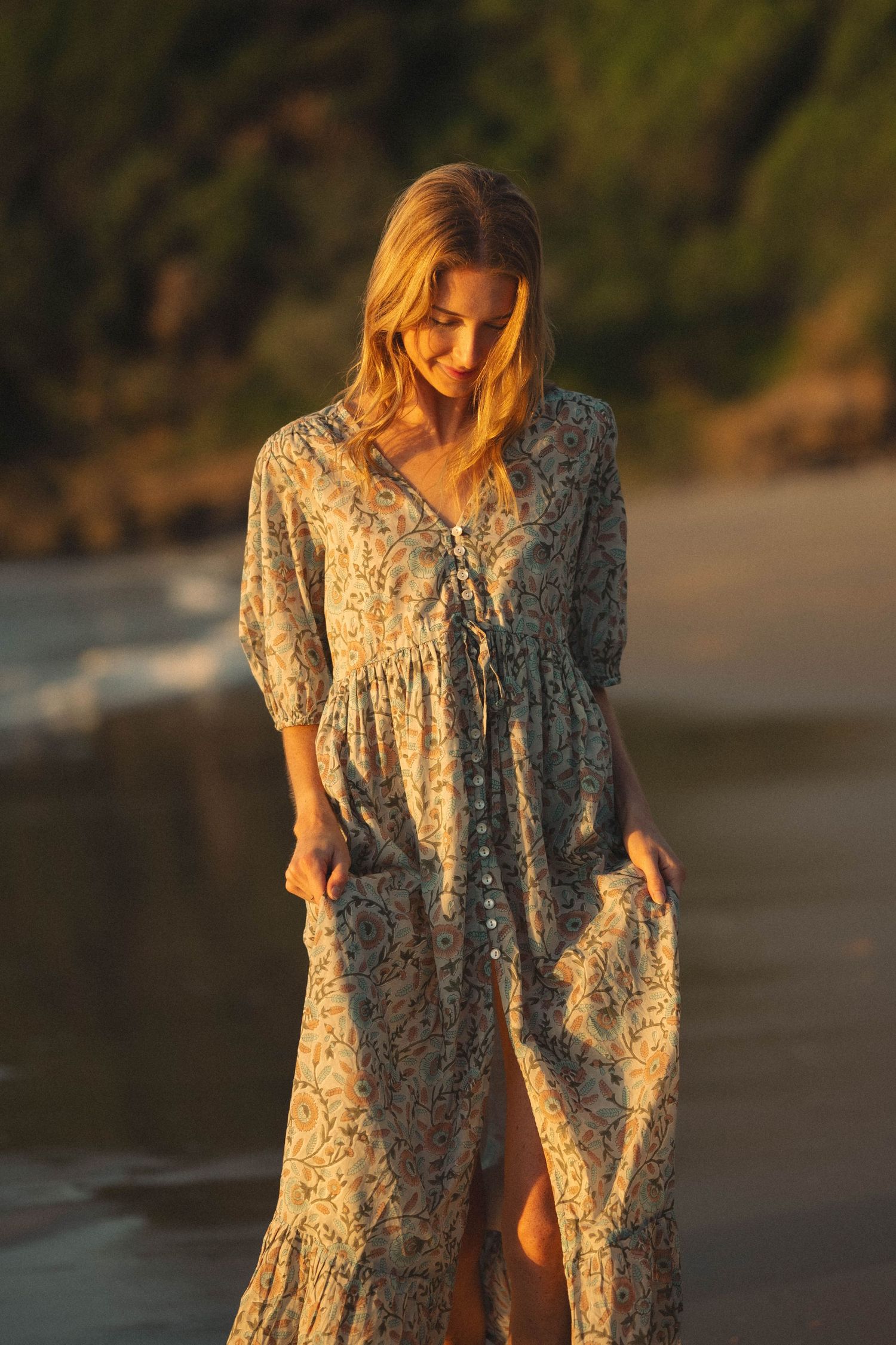 Woman in floral boho maxi dress on beach at golden hour sunset.