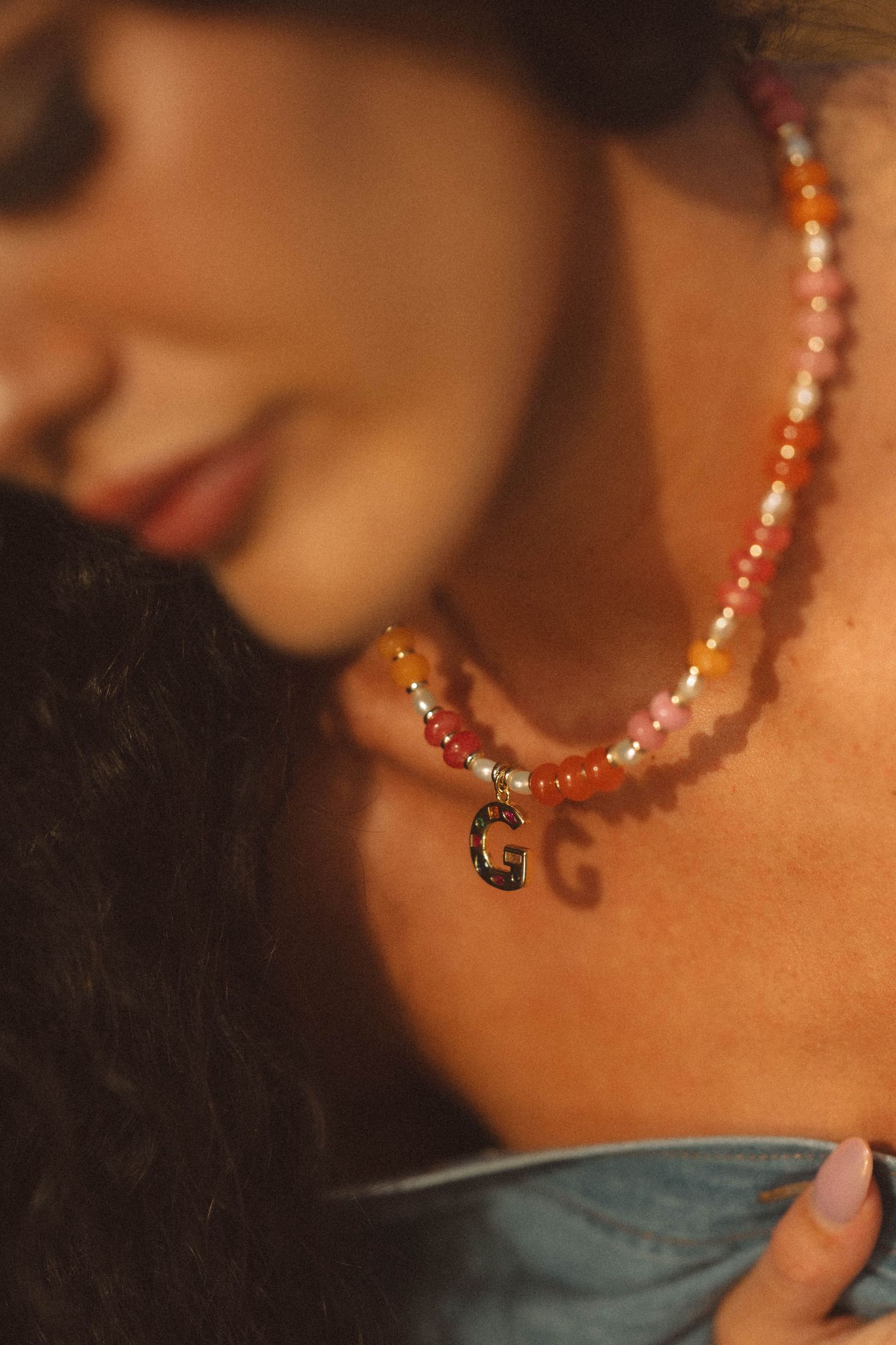 Close-up of colorful beaded necklace with gold letter G pendant worn by a woman.