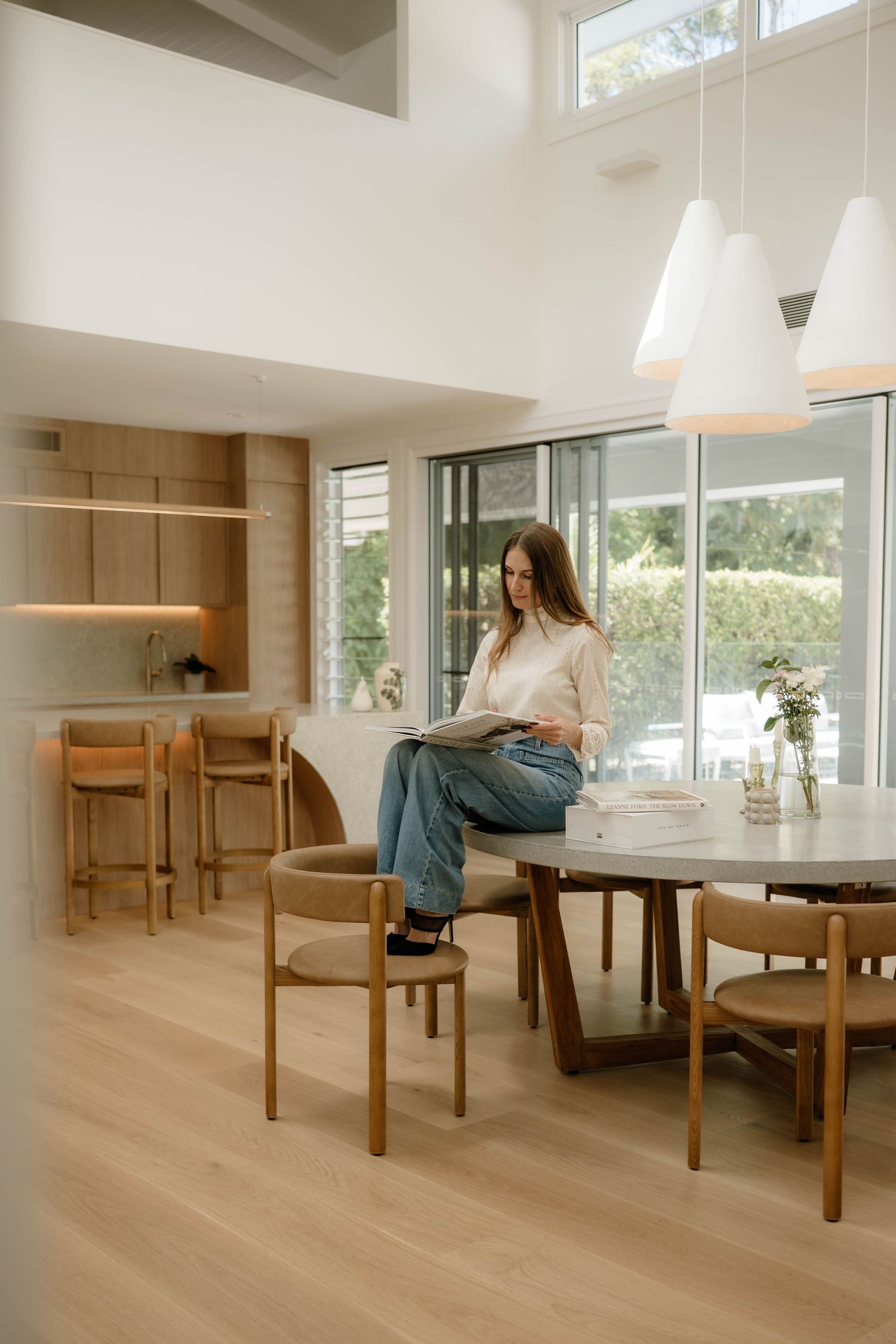 Woman reading a magazine on a dining table in a bright, minimalist open-plan home.