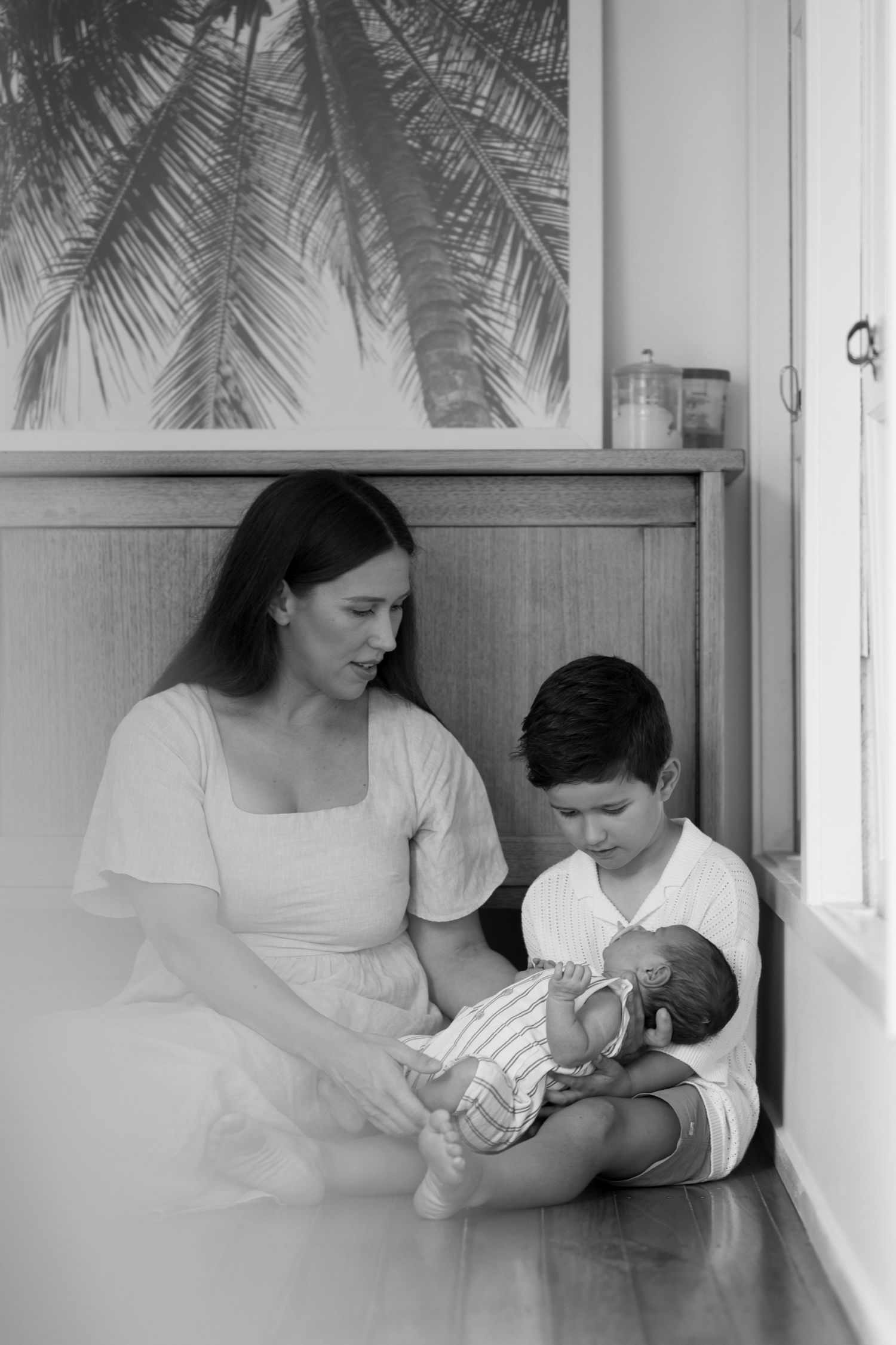 Black and white photo of mother and young boy tenderly holding newborn baby indoors.