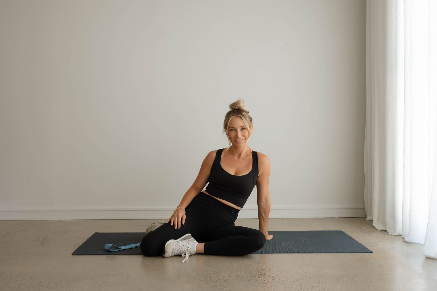 Smiling woman in black activewear sitting on a yoga mat with resistance band.