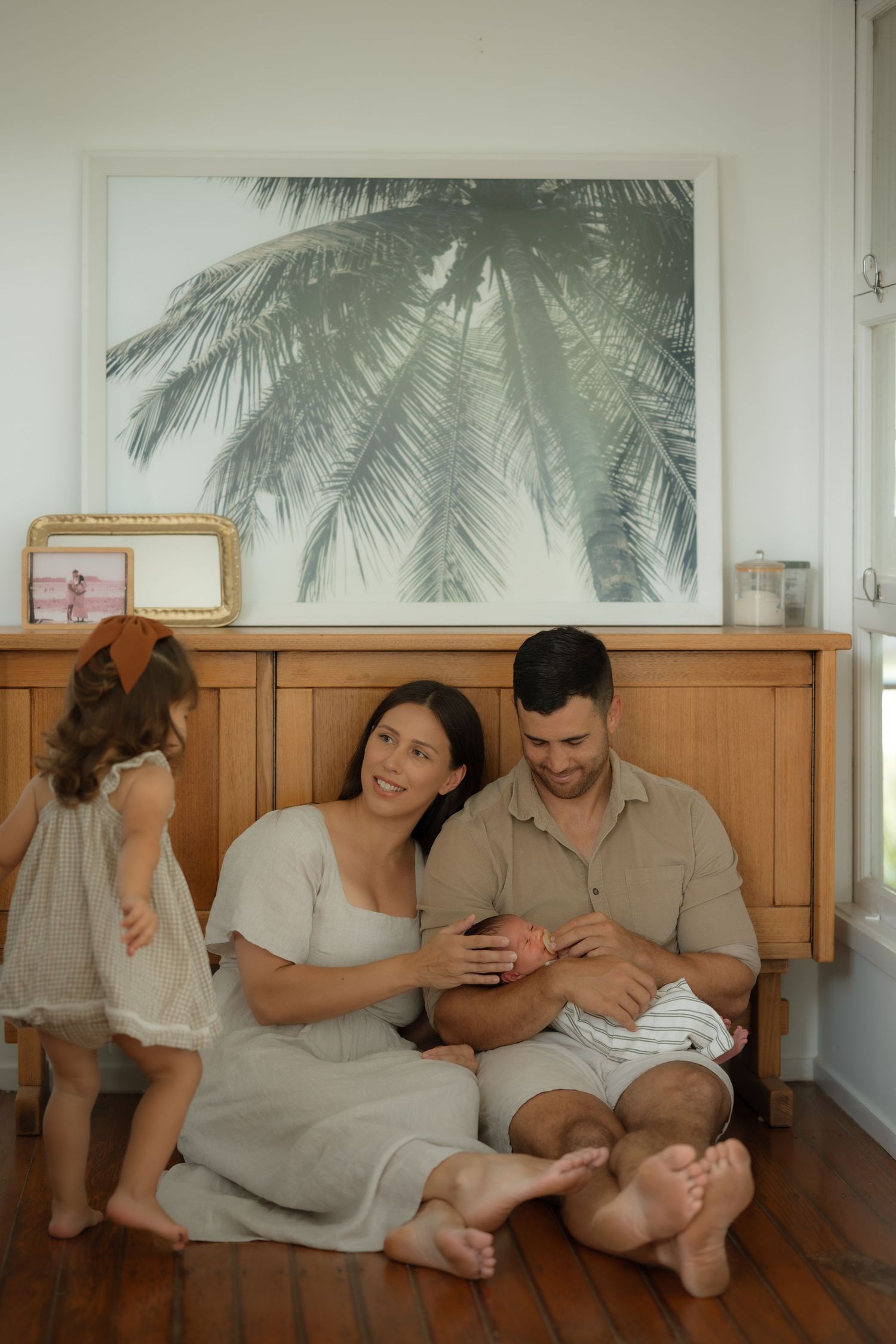 Happy family sitting on hardwood floor with newborn baby and toddler daughter at home.