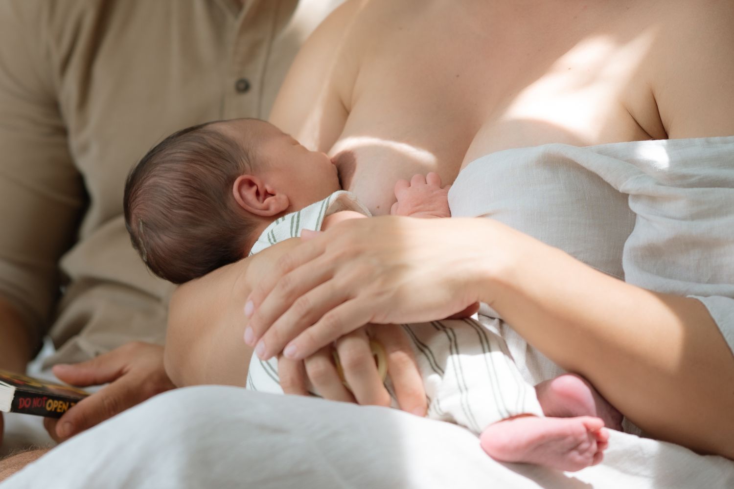 Close-up of mother breastfeeding newborn baby with fathers hand gently supporting infant.
