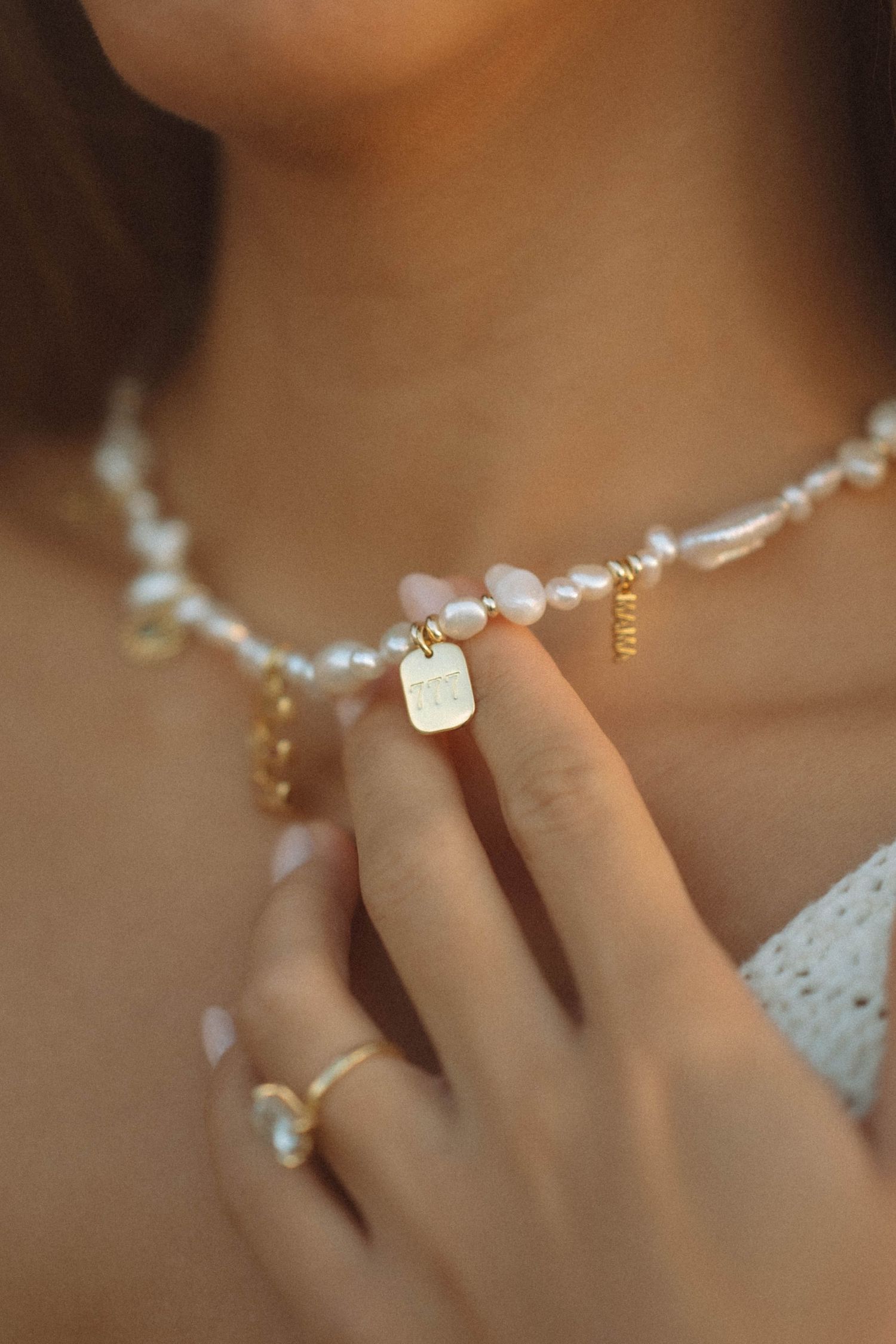 Pearl and rose quartz choker necklace with gold tag charm, styled with gold rings on a woman.
