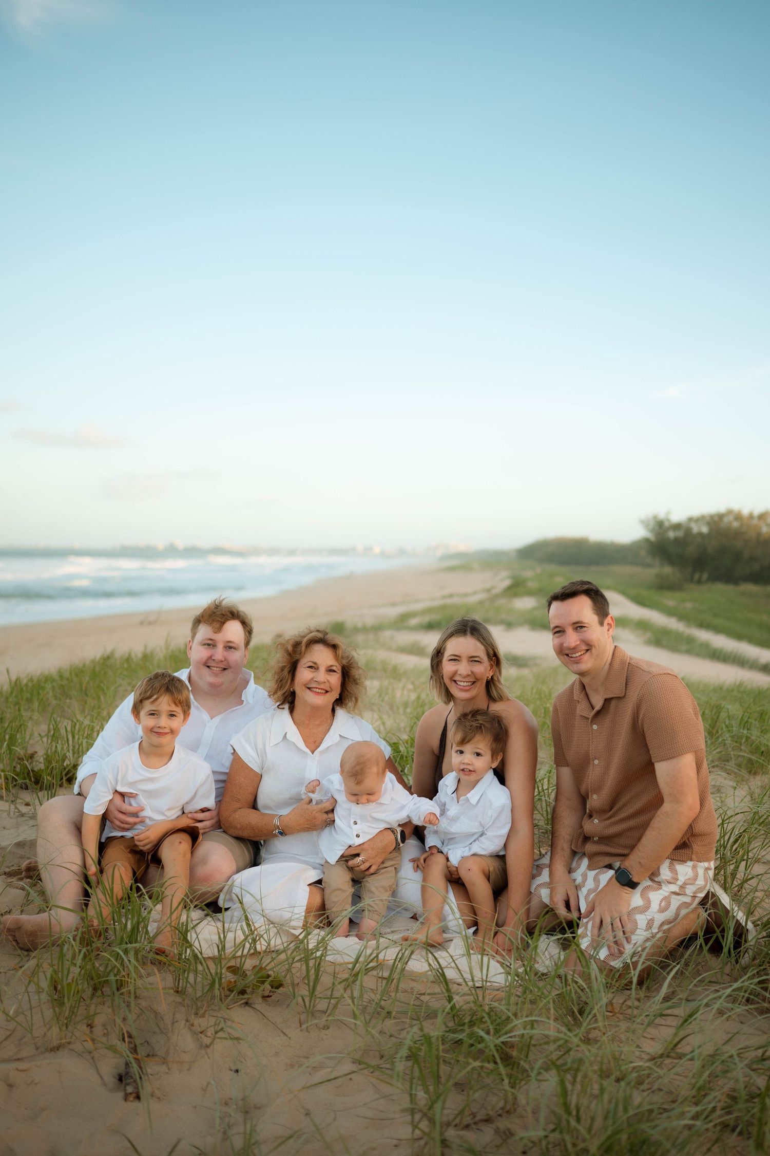 Extended family of seven posing together on sandy beach dunes at golden hour.