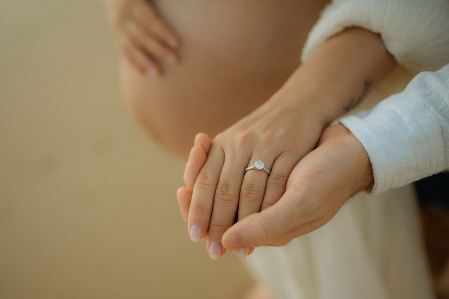 Close-up of couple holding hands showing diamond engagement ring near pregnant belly.