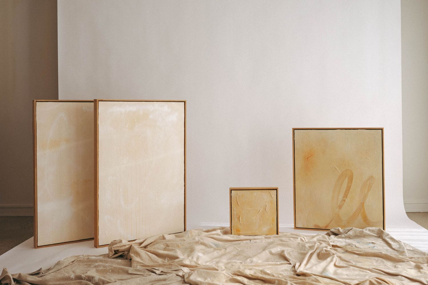 Four framed canvases with golden amber stains lean against a white wall on crumpled brown paper.